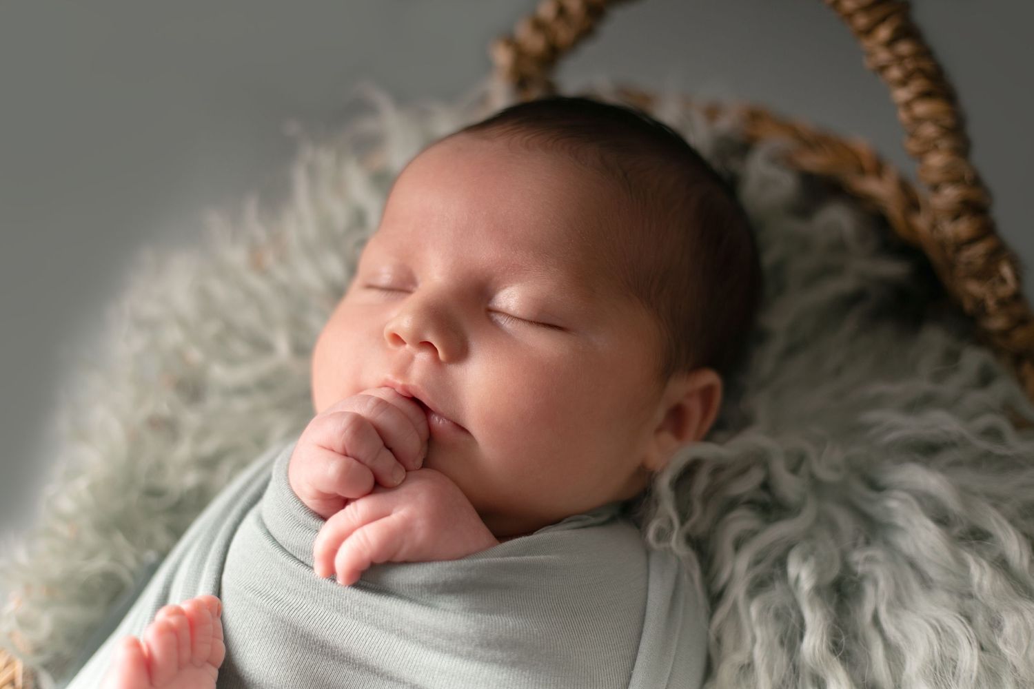 Sleeping newborn baby wrapped in soft white blanket lying on textured white fabric.