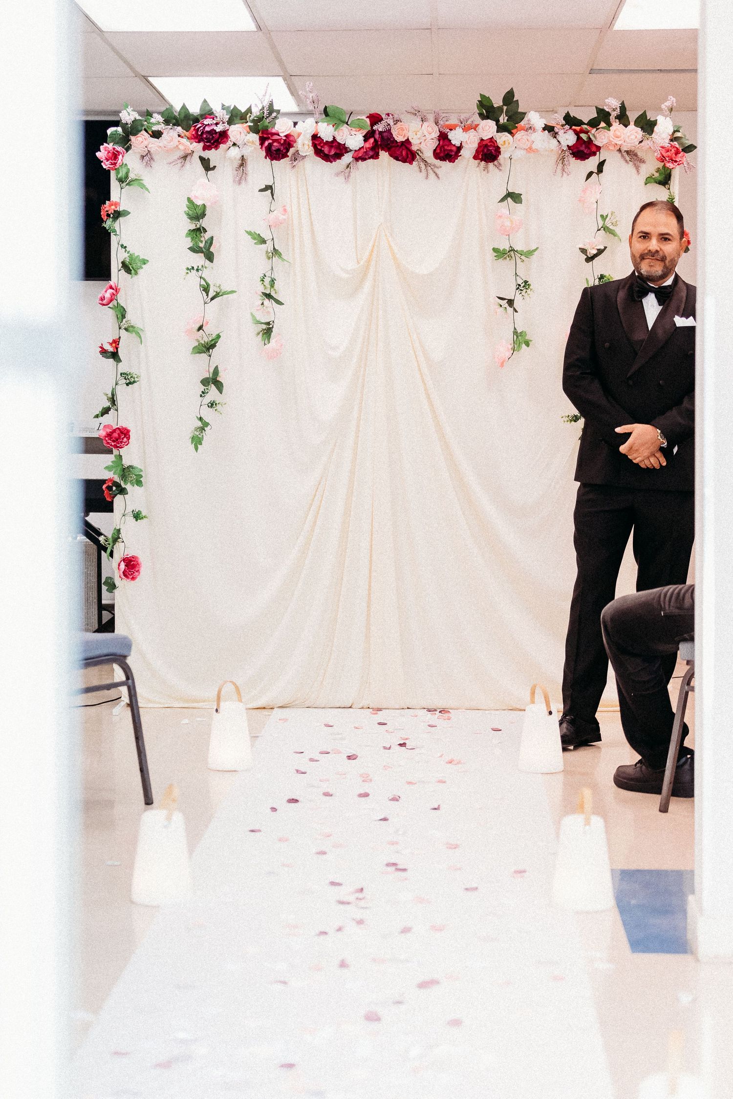 Indoor wedding ceremony setup with white draping and pink floral arch decorations.