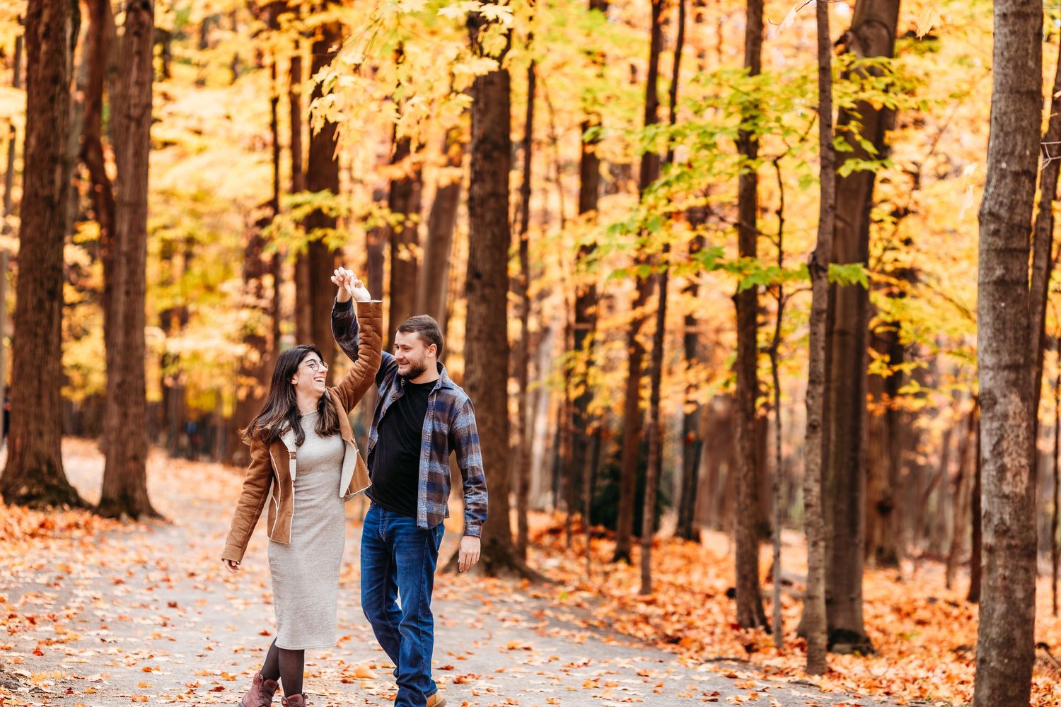 Un couple danse dans une forêt d'automne baignée de soleil, où des feuilles dorées jonchent le sol.