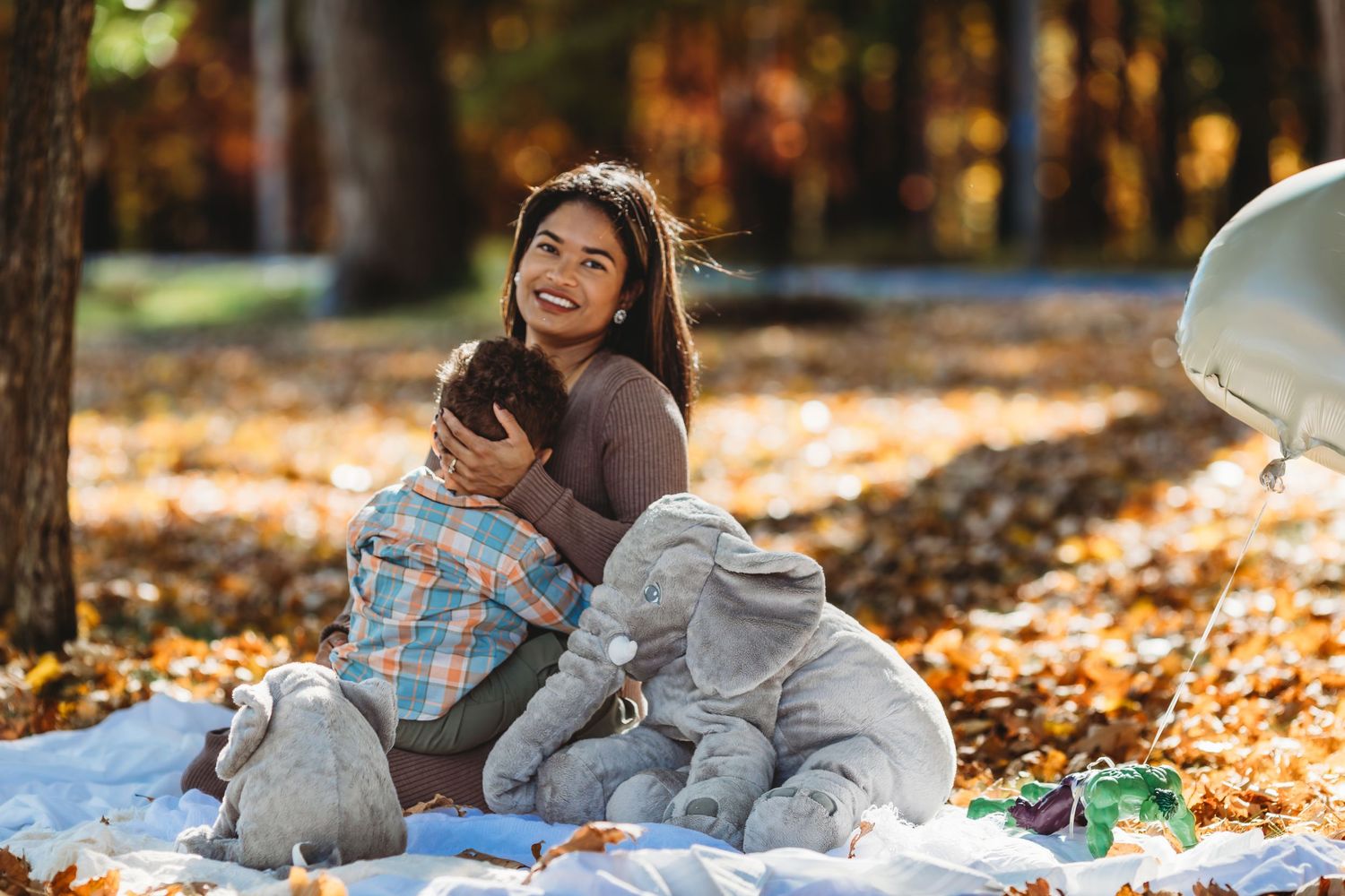 Family relaxing on blanket during fall photoshoot surrounded by autumn leaves.
