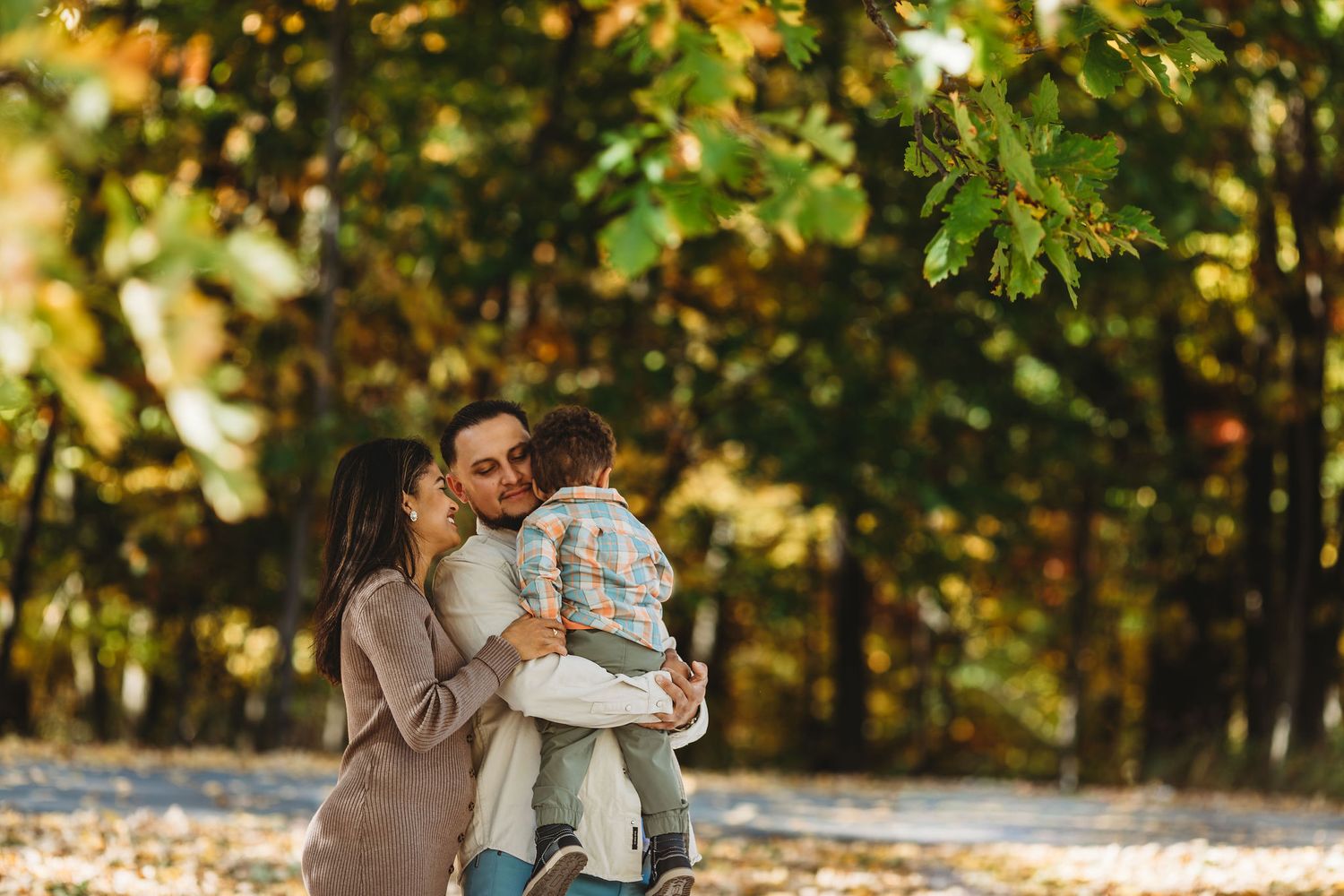 A parent and child share a tender moment while standing in a sunlit autumn forest setting.
