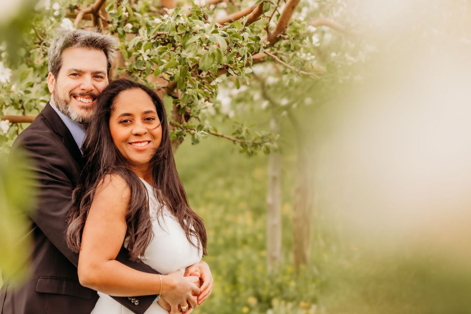 Un portrait romantique en extérieur d'un couple enlacé sous les branches fleuries d'un arbre printanier, baigné d'une douce lumière naturell