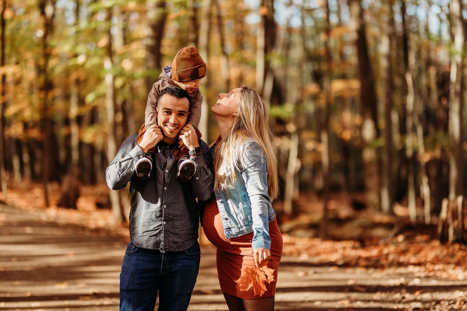 A couple shares a romantic moment together while walking through a sunlit autumn forest with fallen leaves.