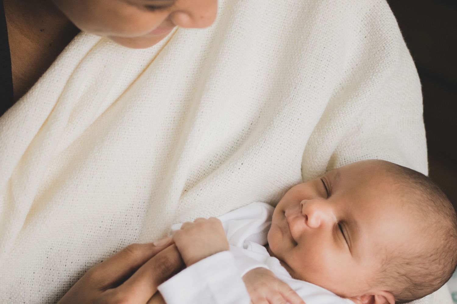 Nouveau-né paisiblement endormi dans les bras de sa maman, enveloppé dans de douces couvertures blanches.
