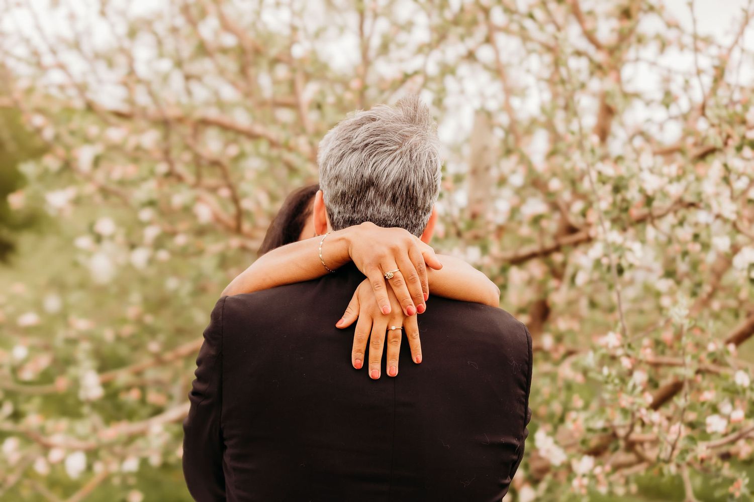 A couple embraces in front of blooming cherry blossom trees during spring.