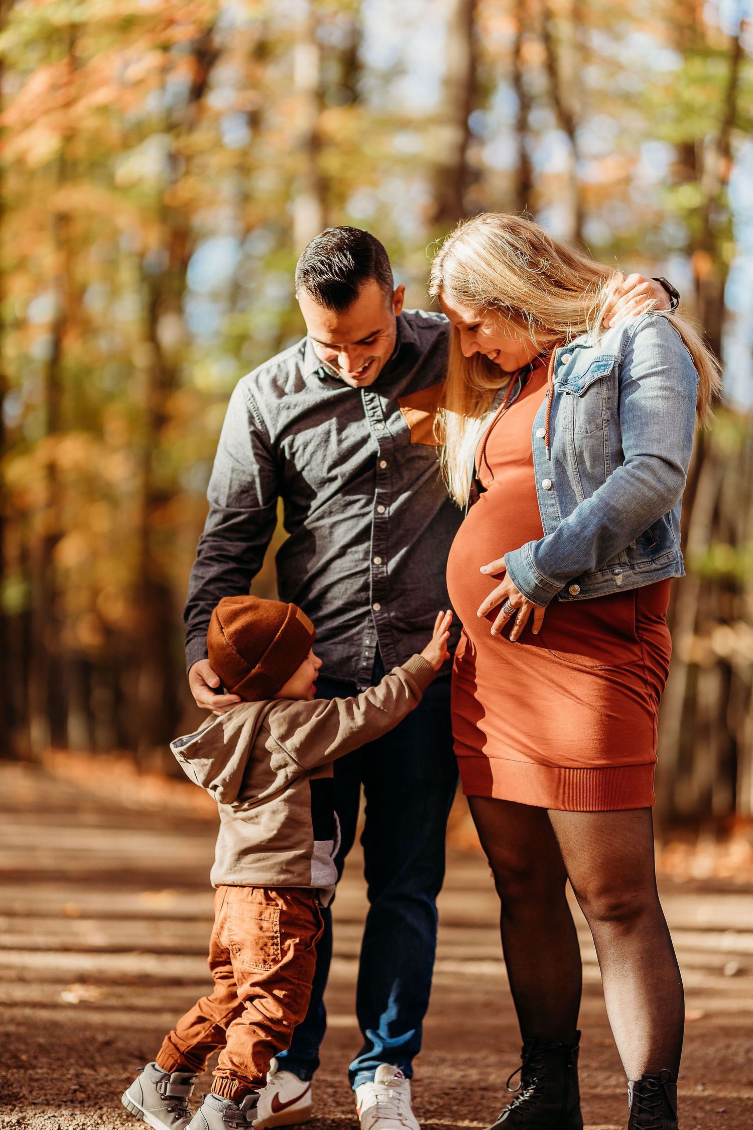 A family plays together outdoors in autumn, bending down and sharing a playful moment in the woods.