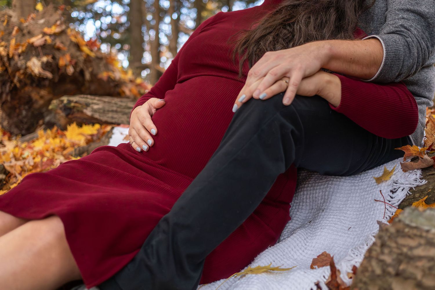A couple snuggles together on a white blanket surrounded by autumn leaves in an outdoor setting.