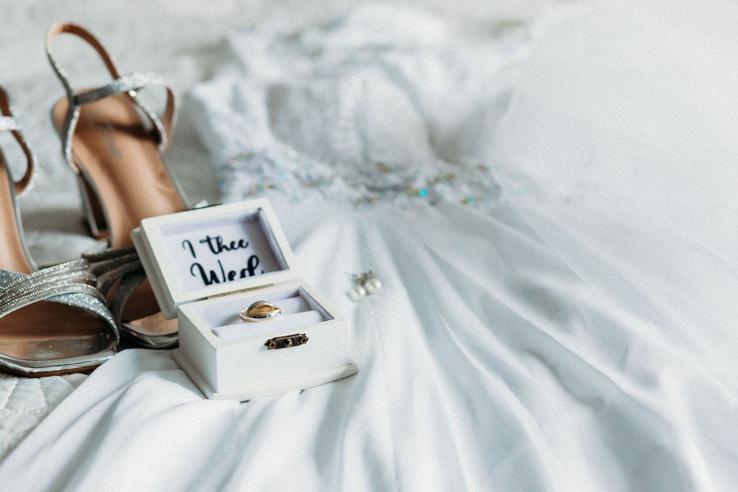 Wedding accessories including shoes and ring box arranged on white tulle fabric.