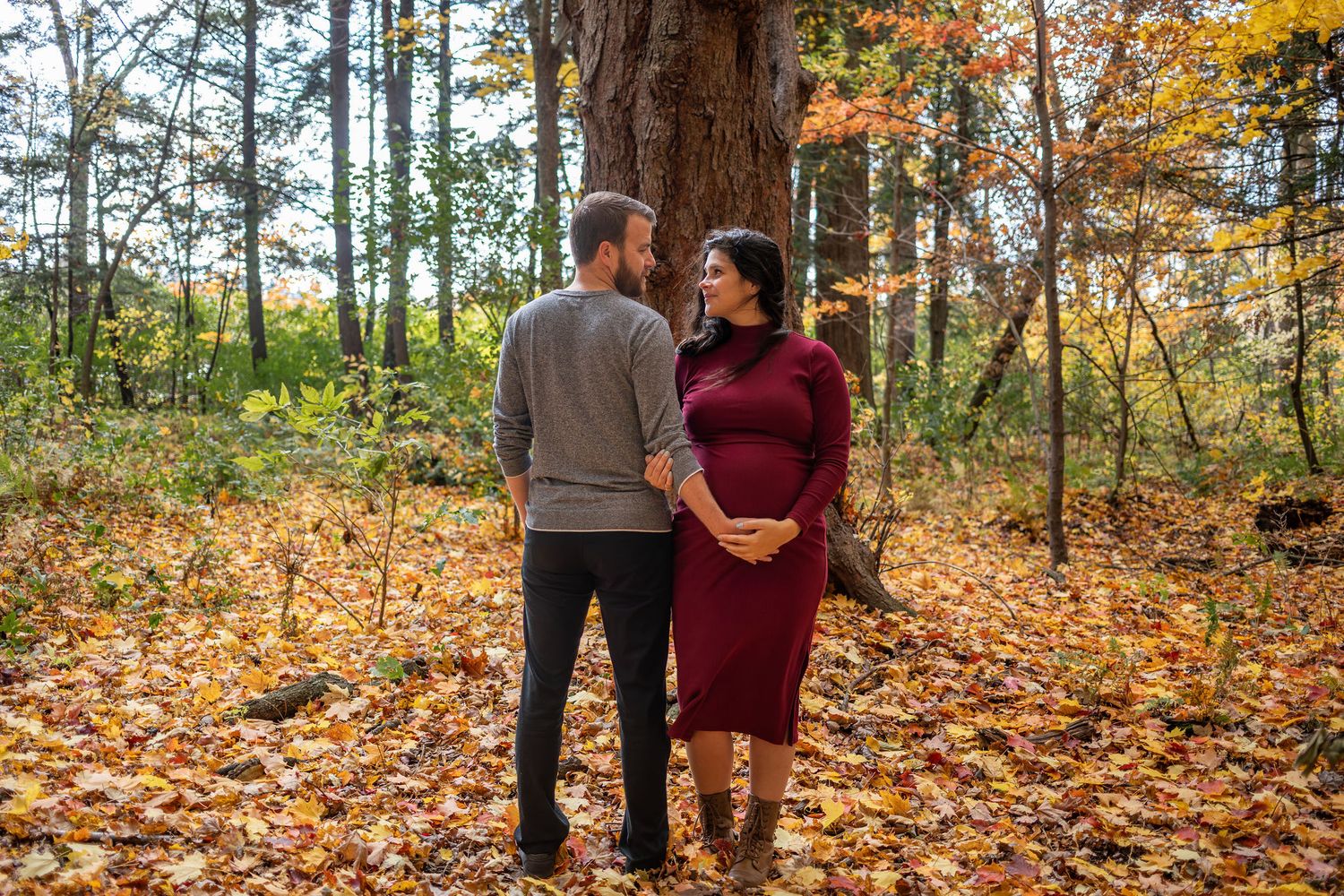 A couple walks together through a colorful autumn forest filled with fallen orange and yellow leaves.
