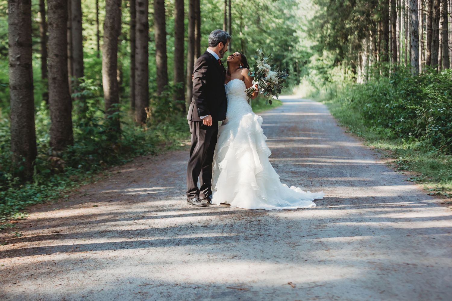 Séance photo de mariage sur un sentier forestier pittoresque, entouré de grands conifères.