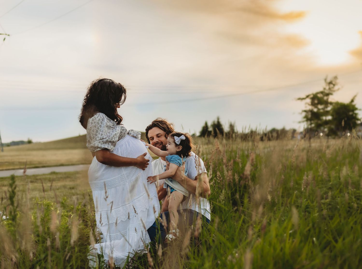 Romantic couple embraces in tall grass field during golden hour sunset in countryside.