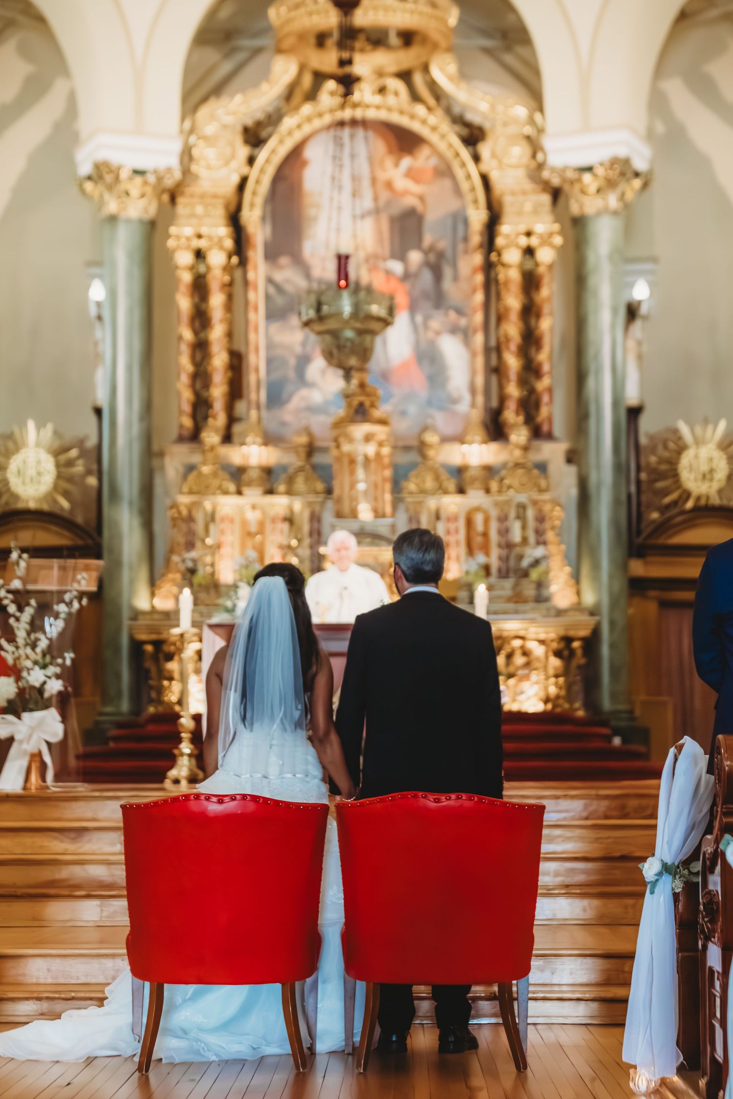 Un couple assis sur des chaises rouges face à l'autel orné de l'église pendant la cérémonie.