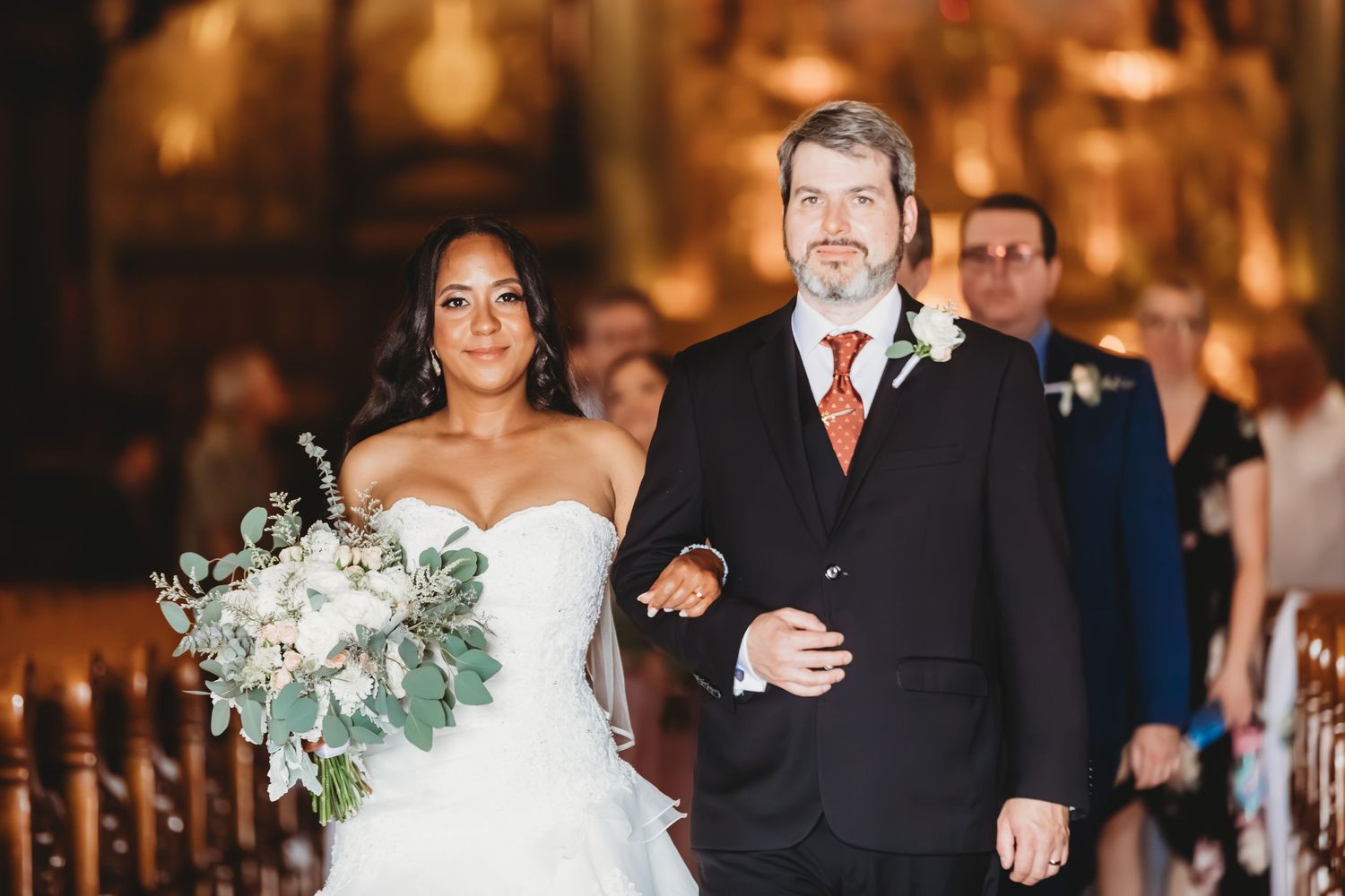 Cortège nuptial dans une église chaleureusement éclairée et élégamment décorée.