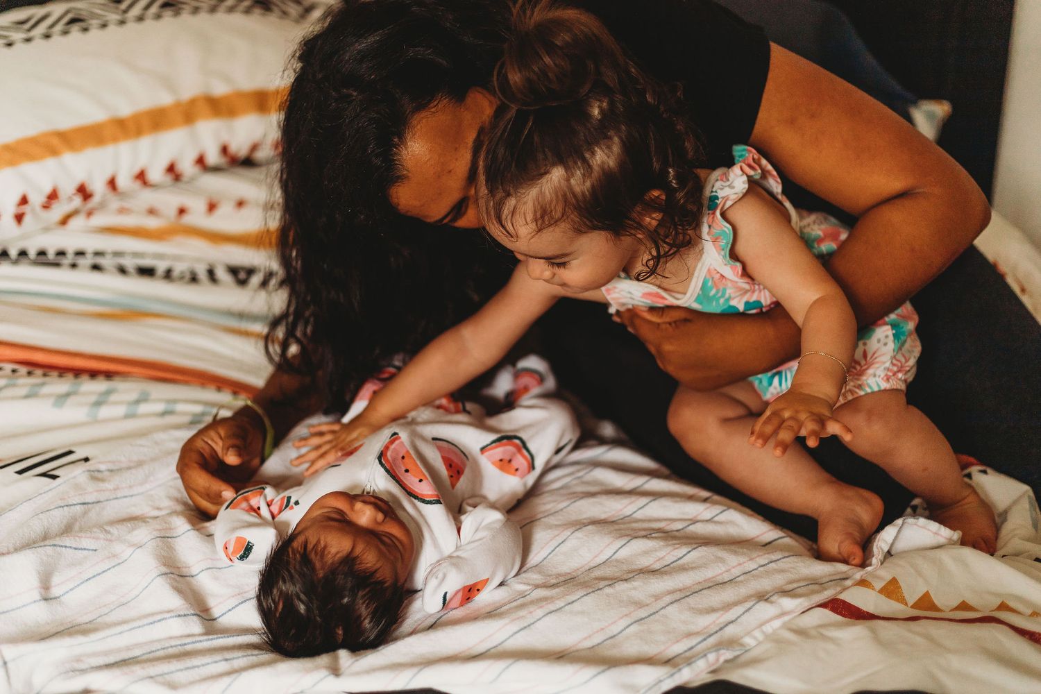 Two children play together on a bed with patterned blankets in a candid moment.