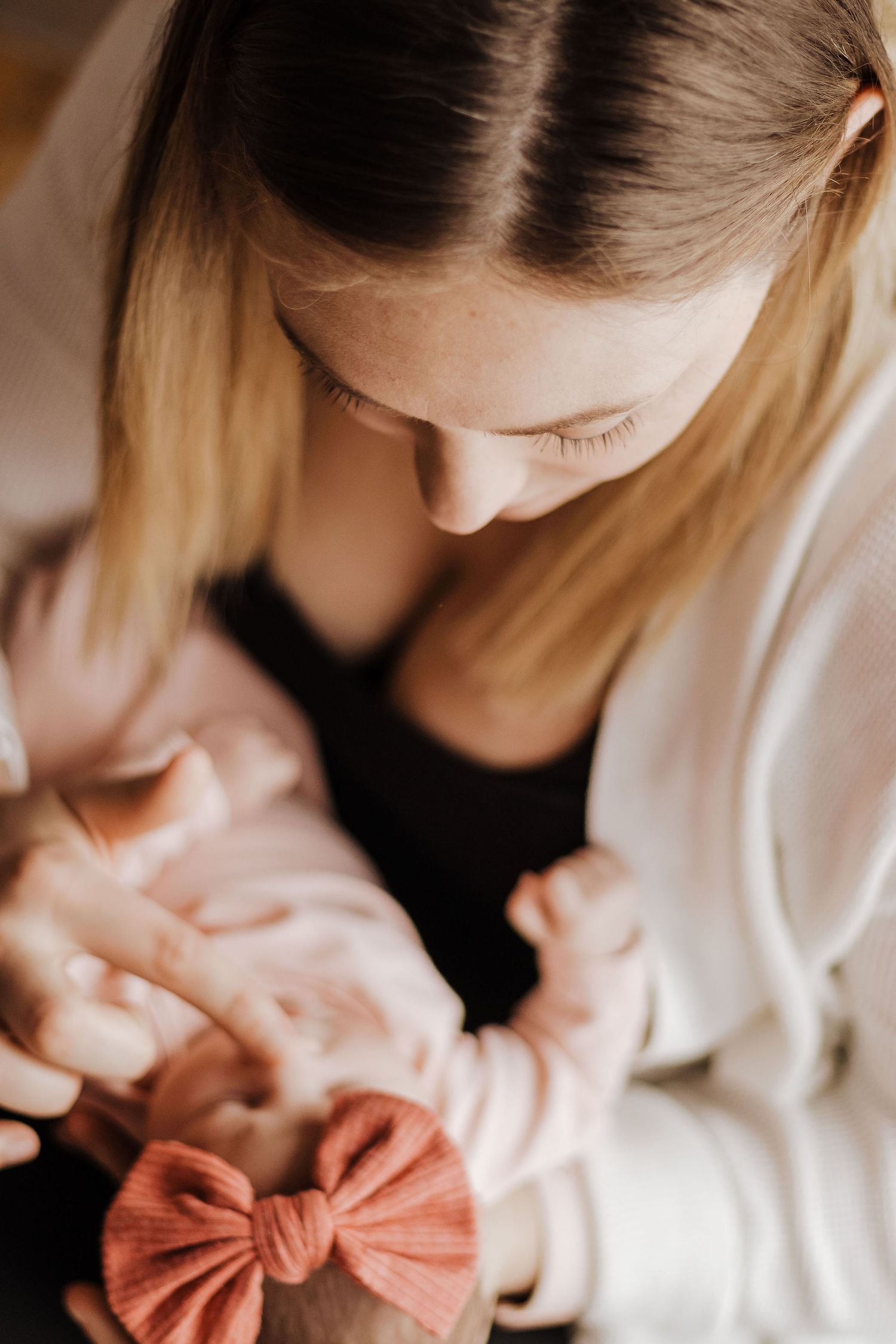A tender moment captured in warm tones as a person in a white cardigan gazes down at a baby wearing a pink bow.