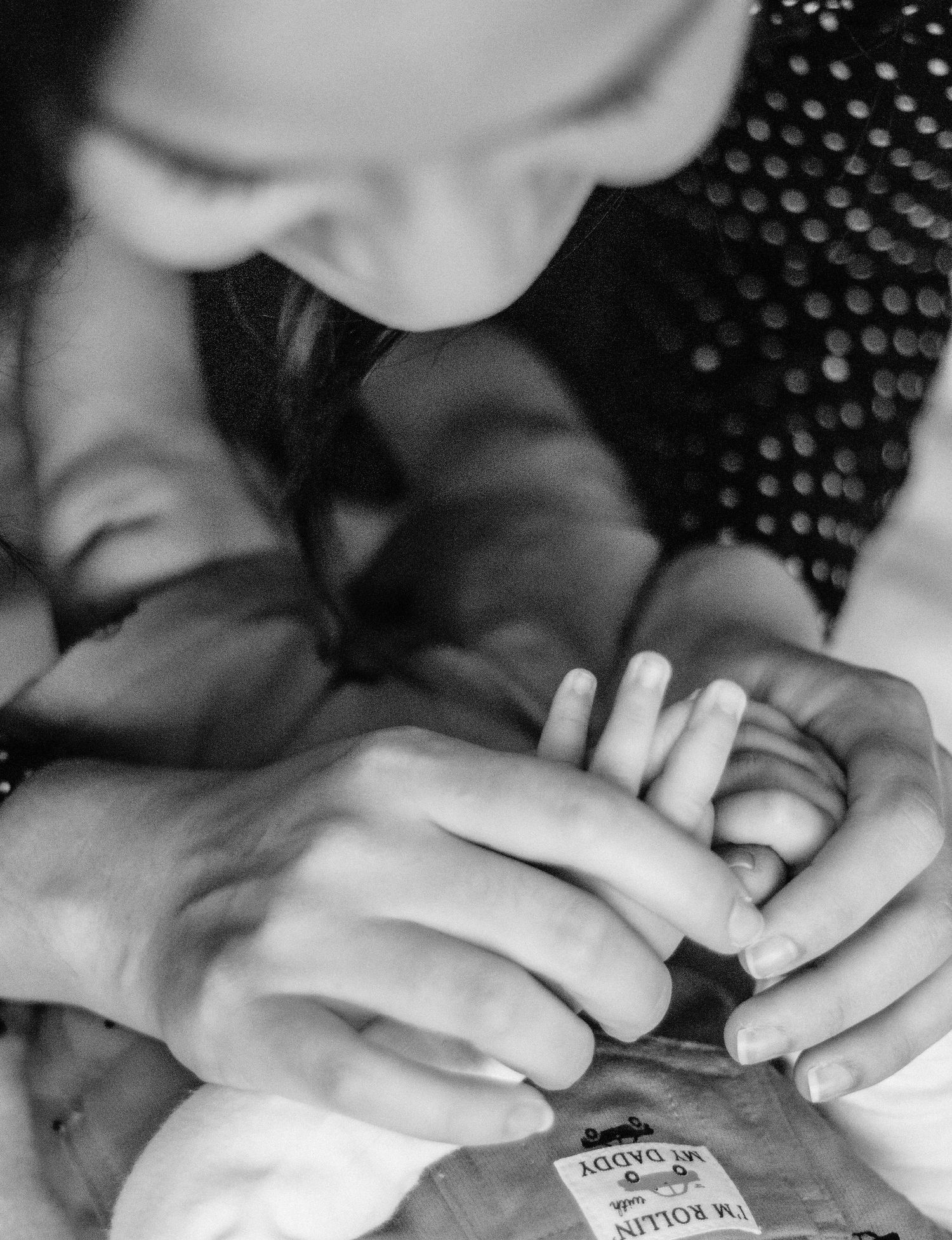 Close-up black and white image of hands delicately handling a small object against a textured background.