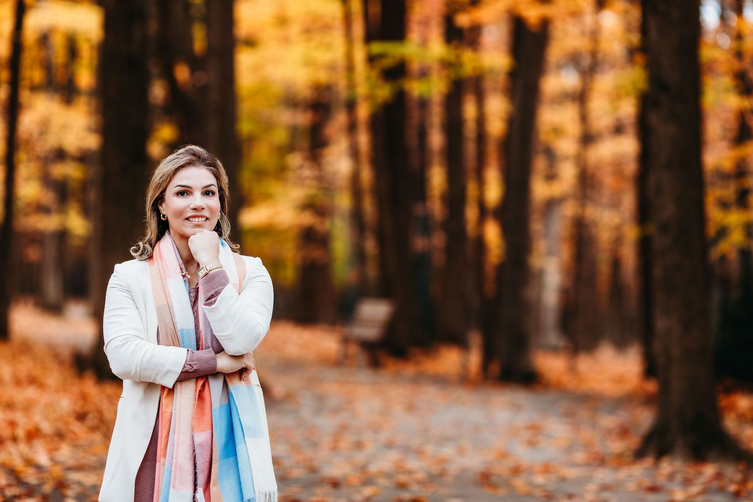 Someone in a white sweater and blue scarf walks through a vibrant autumn forest with golden fallen leaves.