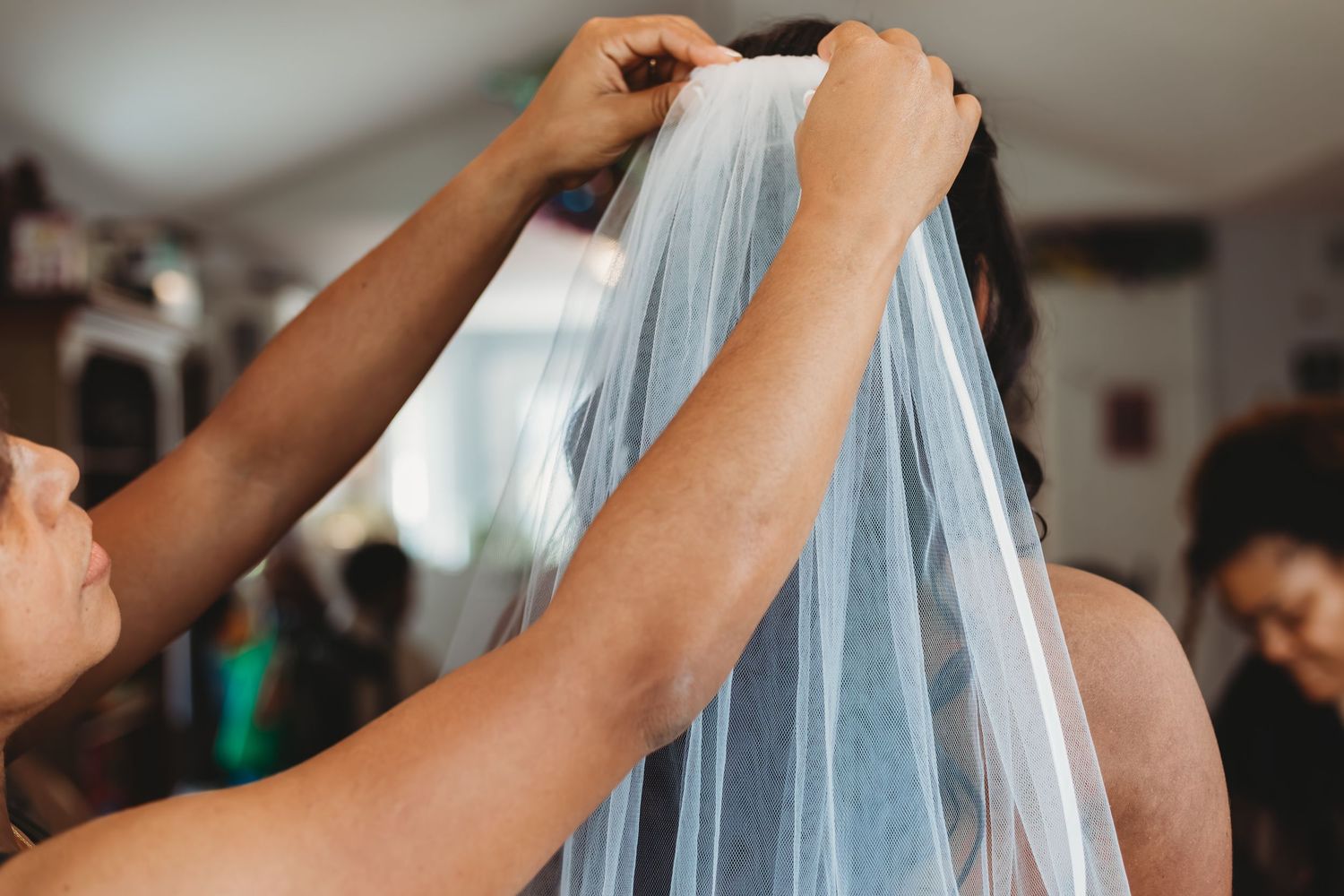 Des mains se lèvent pour tenir et ajuster le voile de la mariée