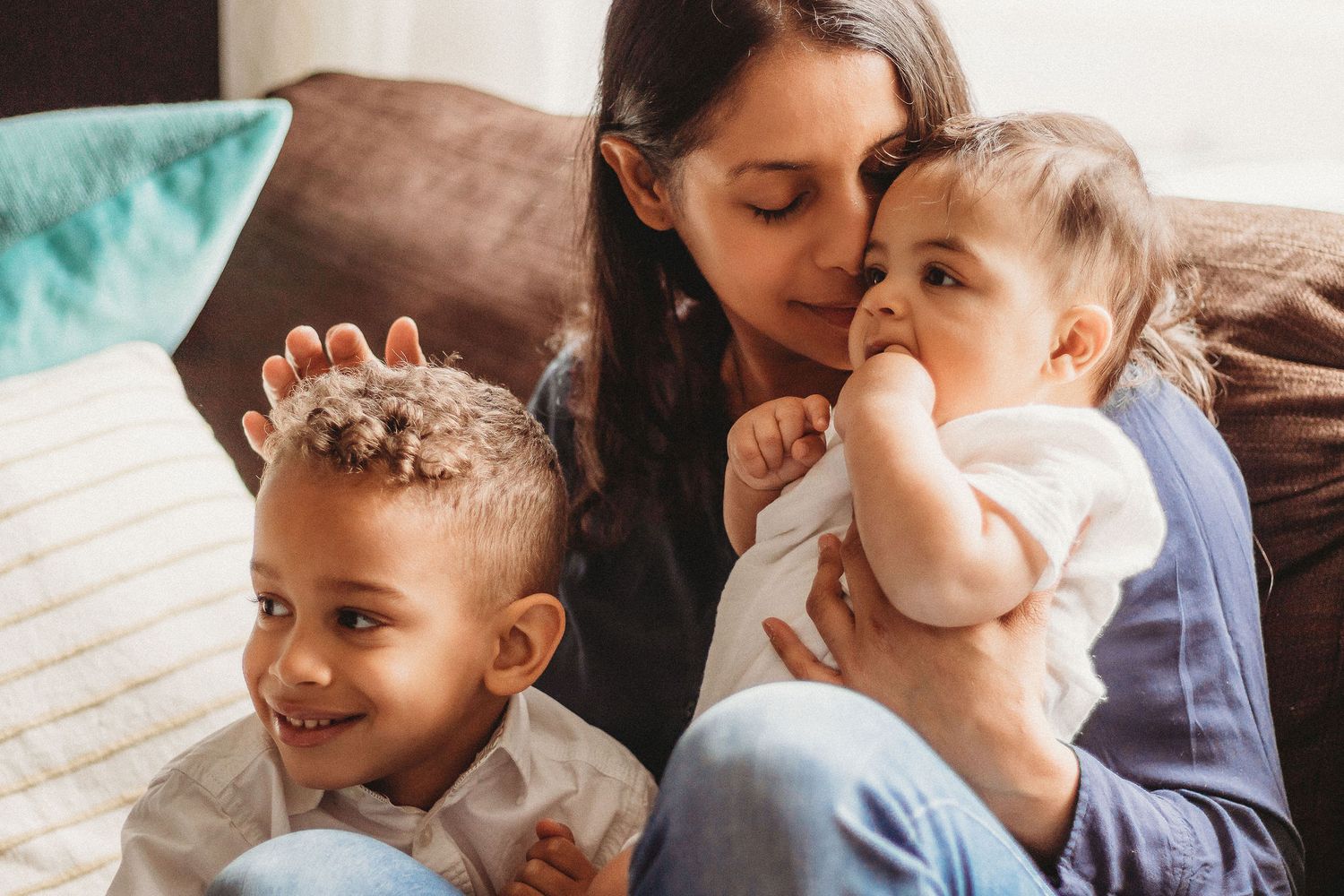 A tender family moment on a brown couch with a teal pillow as they share loving expressions together.