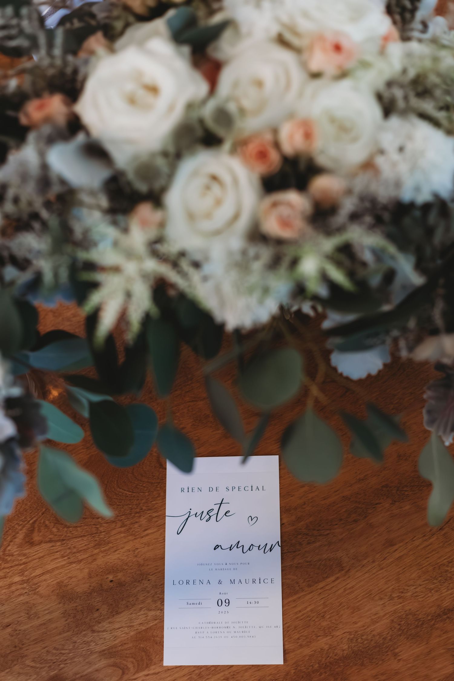 Cartes d'invitation de mariage et compositions florales avec des roses blanches et de l'eucalyptus sur une surface en bois.