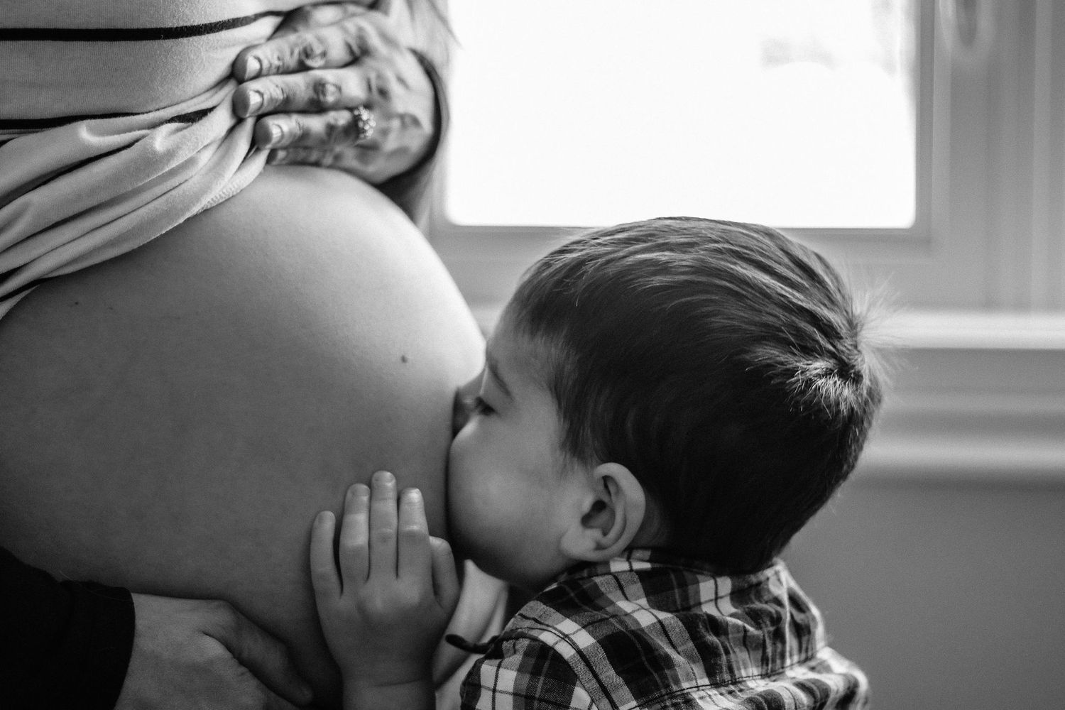 A series of black and white photos showing tender moments between parent and child in window light.
