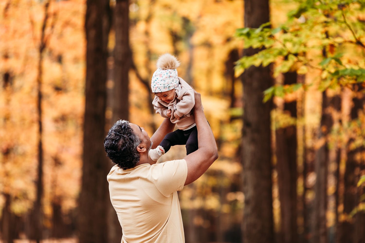 Une photo d'un père et de sa fille profitant d'un moment spontané dans une forêt d'automne ensoleillée aux feuillages dorés.