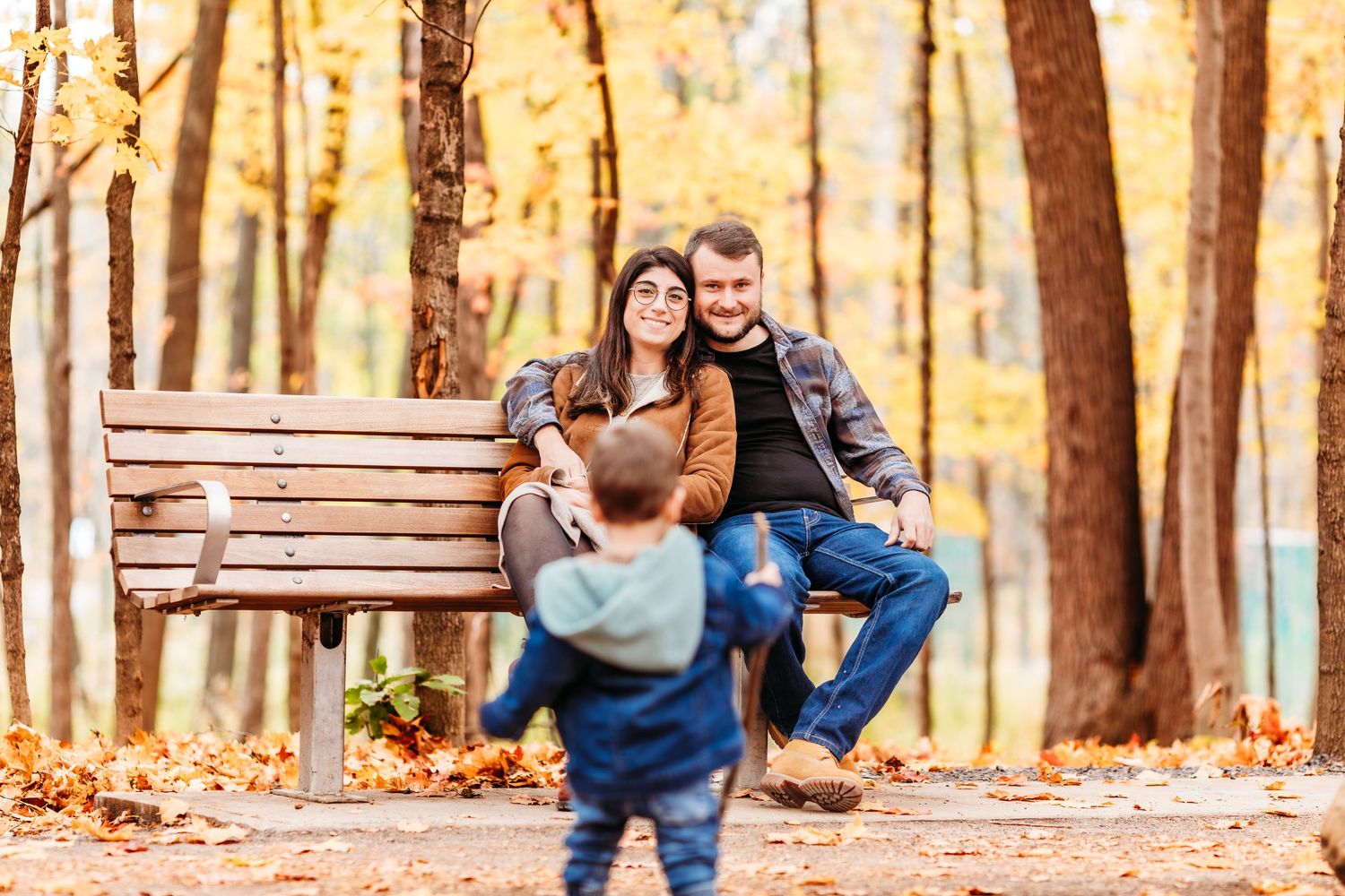 Un couple est assis sur un banc rustique en bois, entouré d'arbres d'automne aux feuilles dorées, dans un parc.