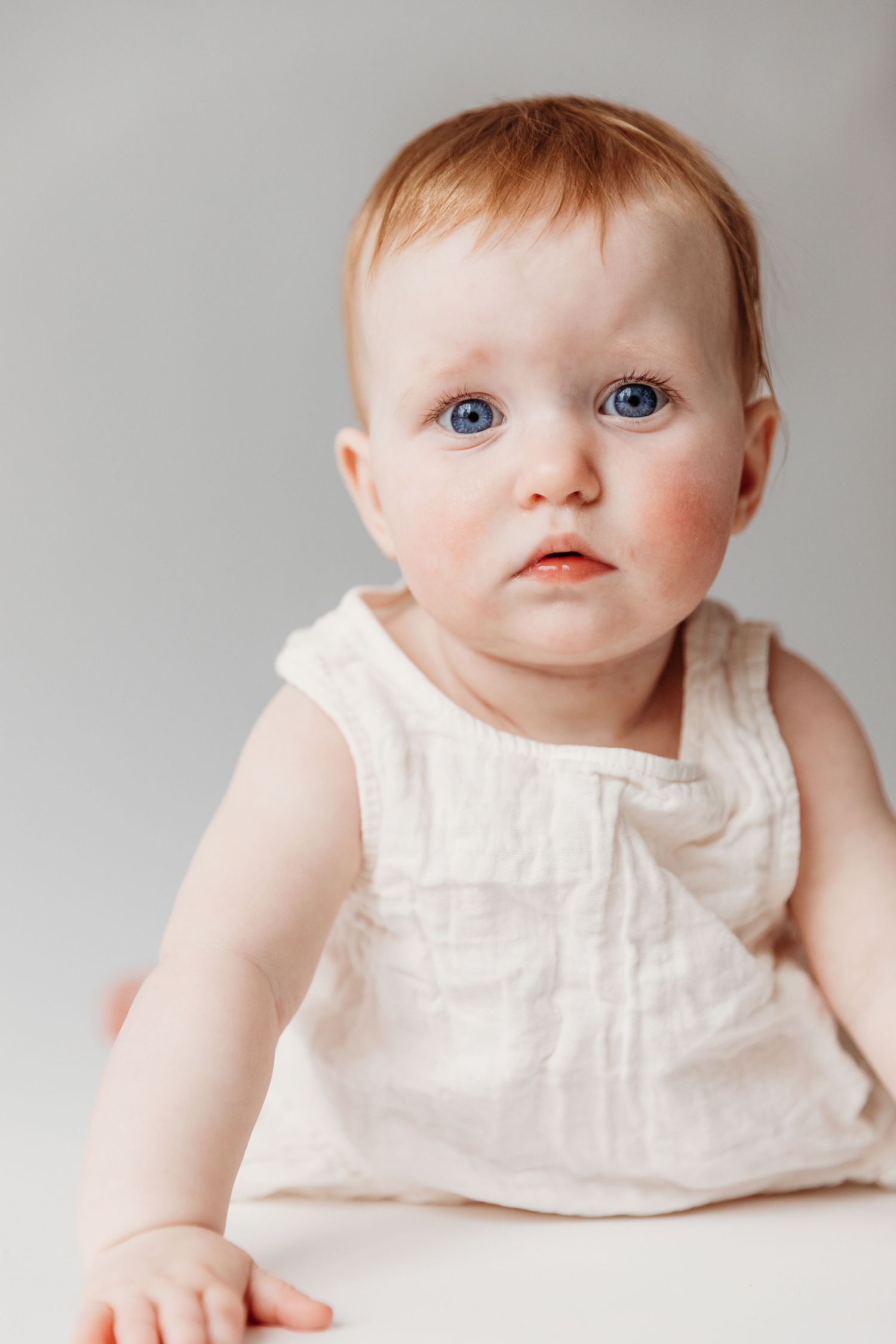 Baby wearing white dress poses for milestone portraits in studio setting.
