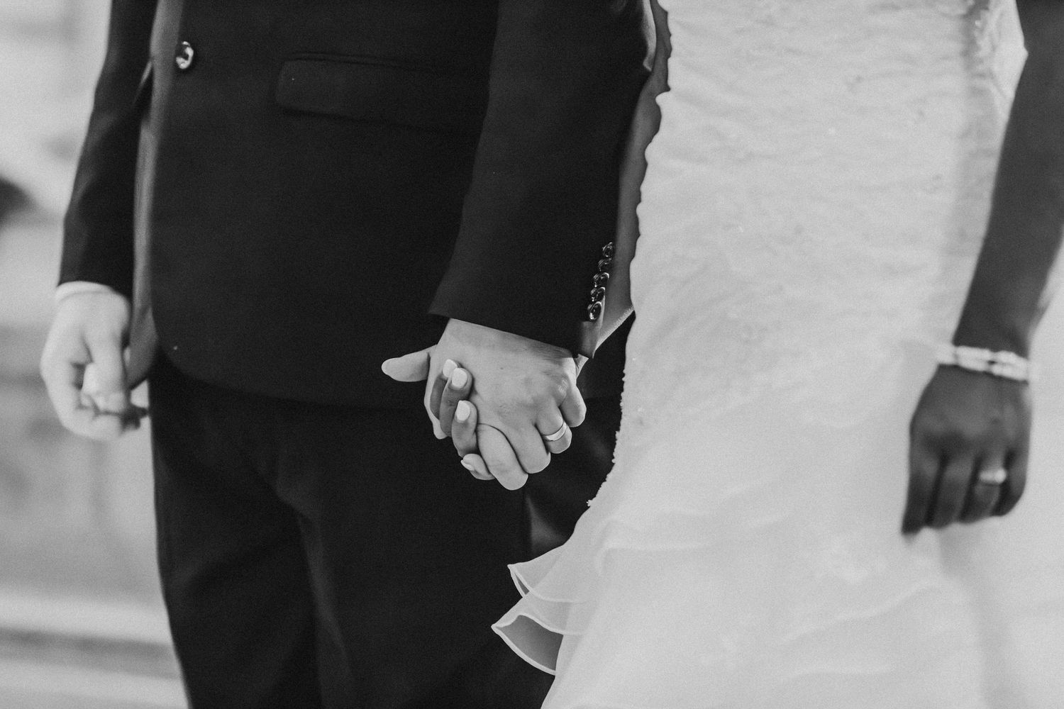 Une photographie en noir et blanc montre des mariés marchant main dans la main sur un chemin.