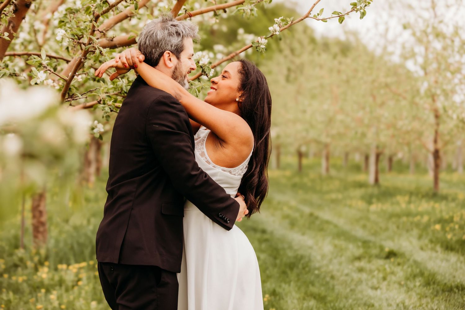 Un couple en tenue de mariage s'embrasse dans un verger baigné de soleil lors de leur séance photo de mariage en extérieur.