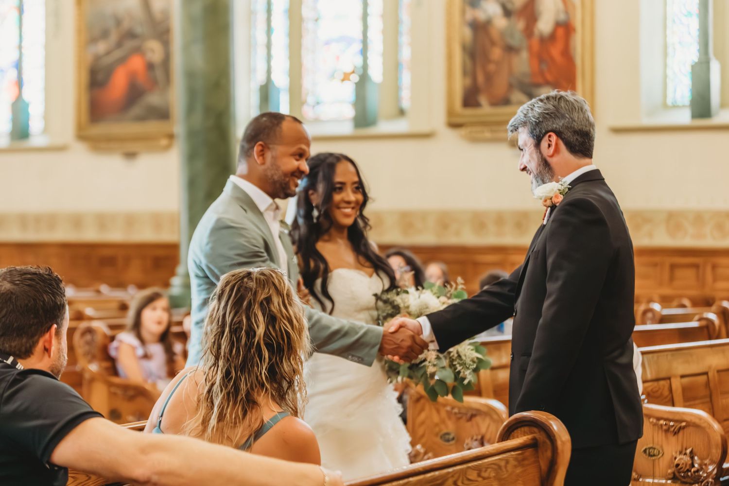 Une joyeuse cérémonie de mariage se déroule à l'intérieur d'une magnifique église ornée de vitraux et d'œuvres d'art religieuses.