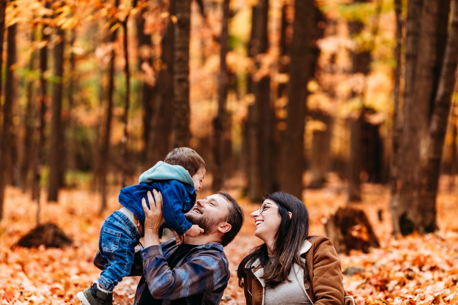 Une famille profite d'une journée d'automne ludique dans une forêt remplie de feuilles mortes orangées.