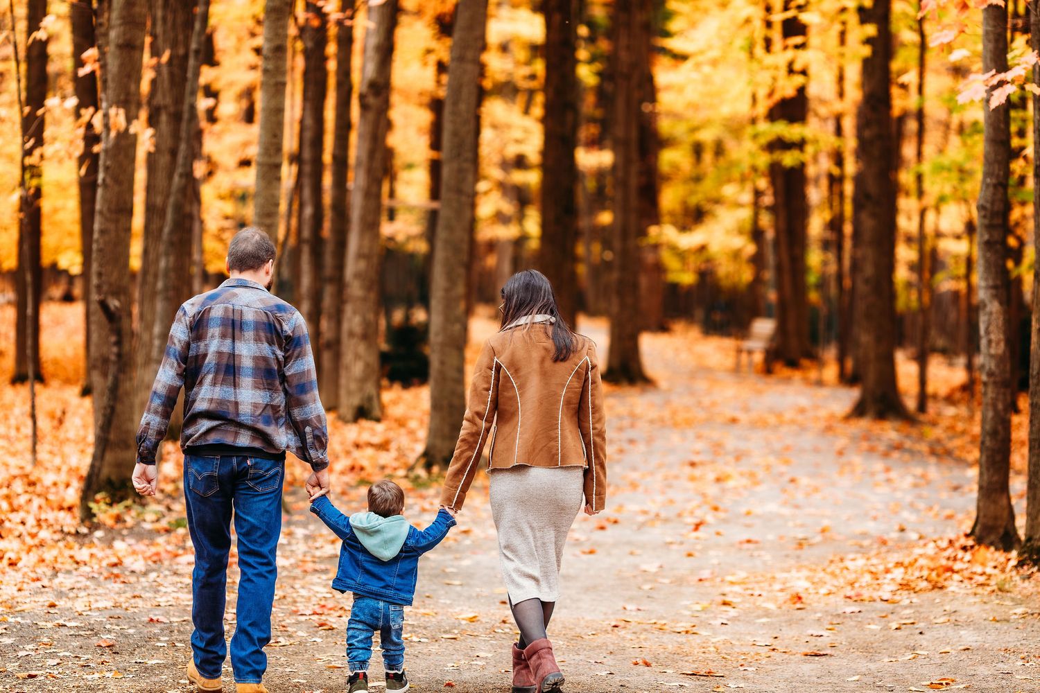 Family walking together on a leaf-covered path through autumn forest during golden sunset.
