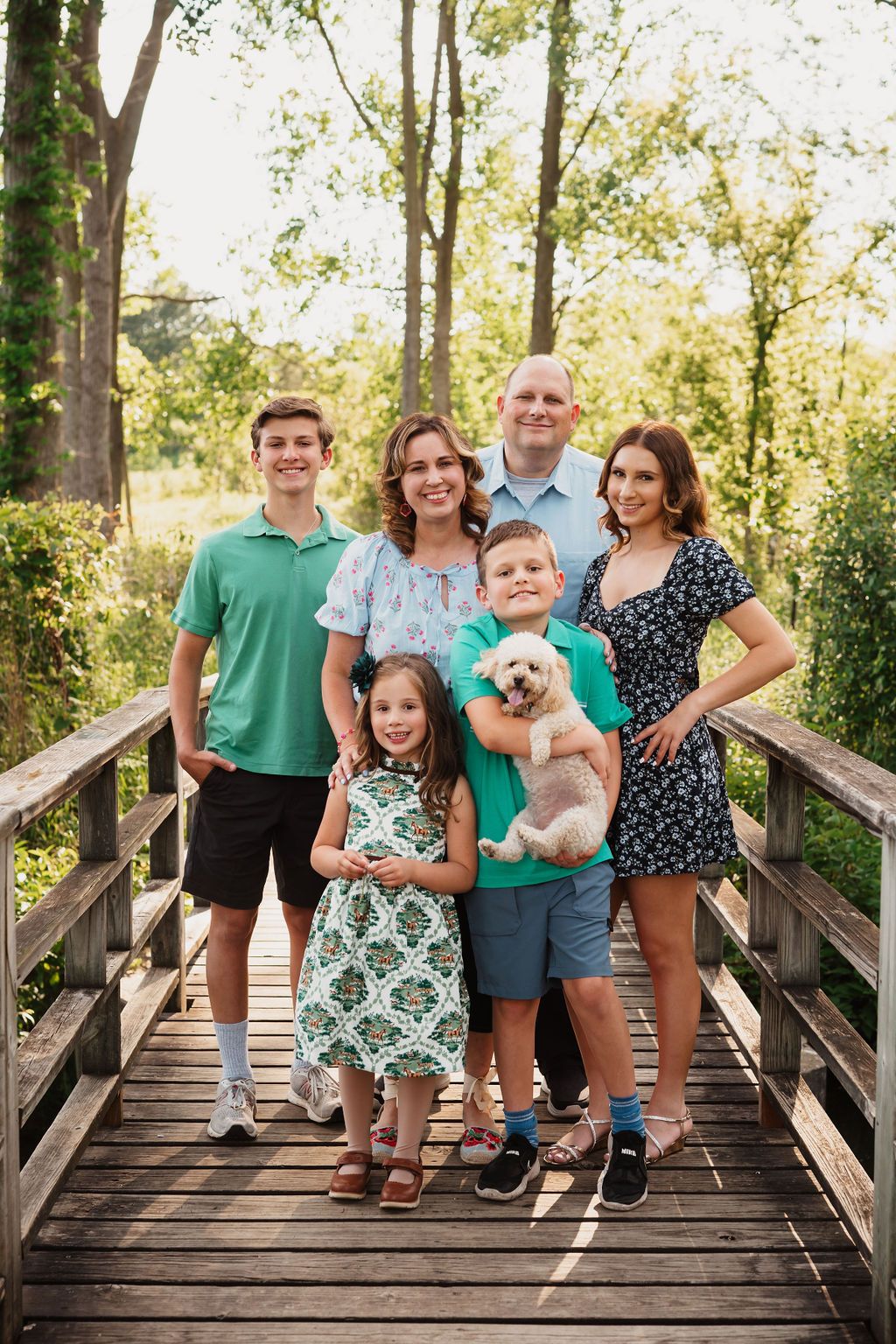 A group poses together on a wooden boardwalk surrounded by green trees on a sunny day.