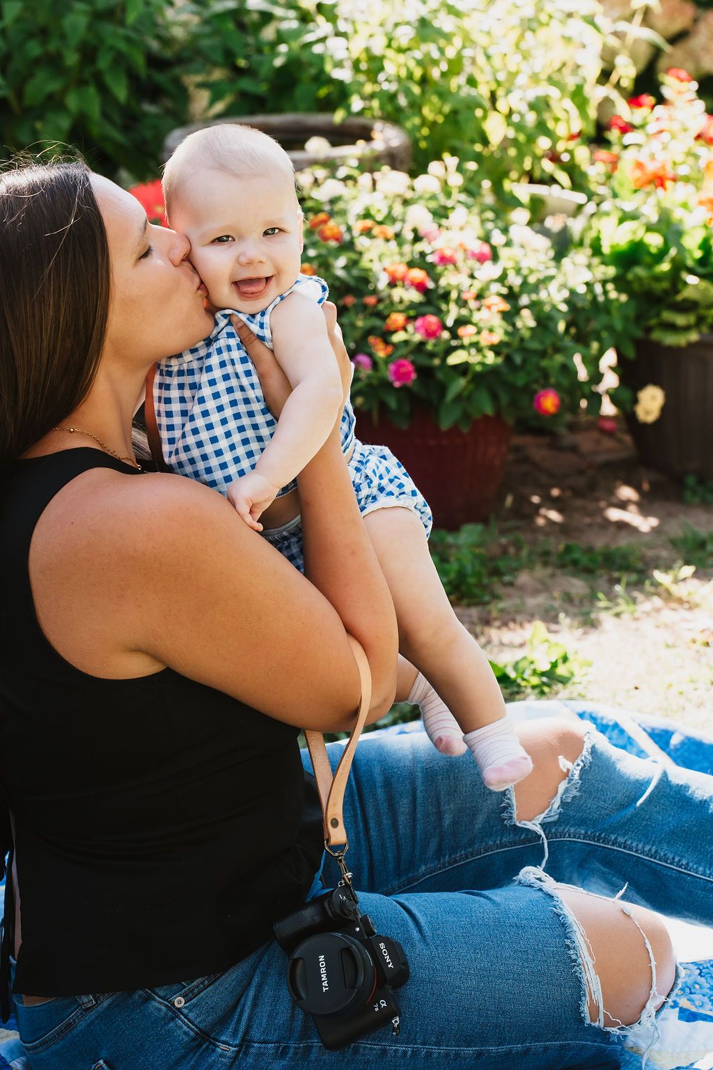 Casual outdoor portrait session with blue gingham outfit details against flowering garden.