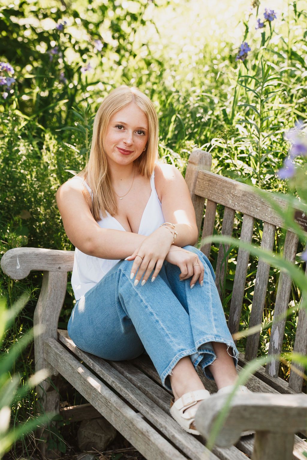 Person relaxing on a wooden garden bench surrounded by greenery.