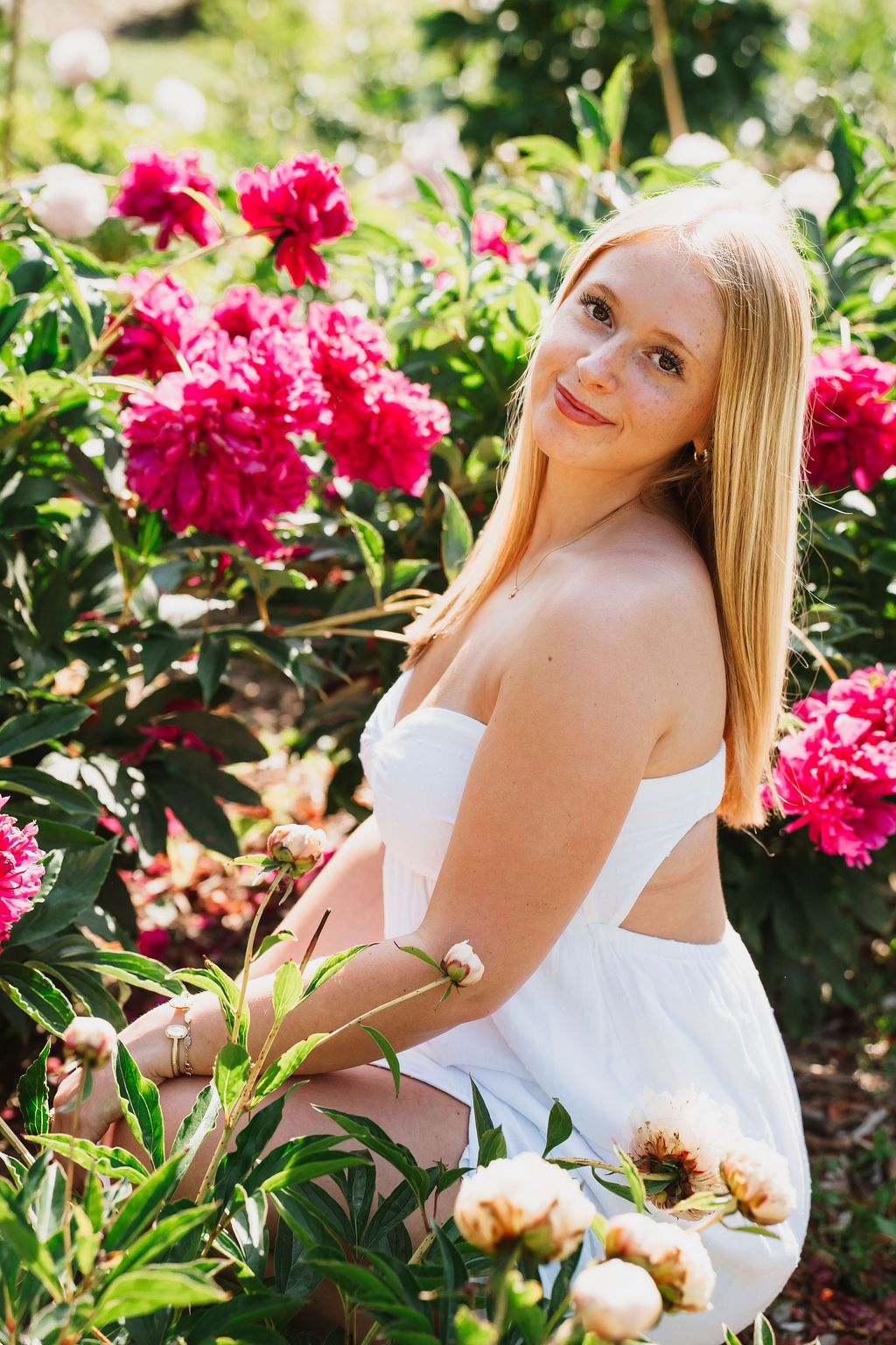 Summer portrait among blooming pink peonies in a garden setting.