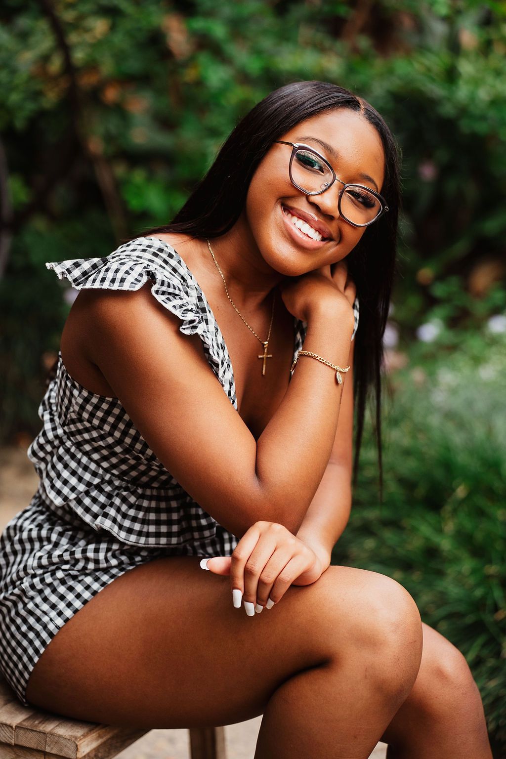 A black and white gingham dress creates contrast against lush greenery in an outdoor portrait setting.
