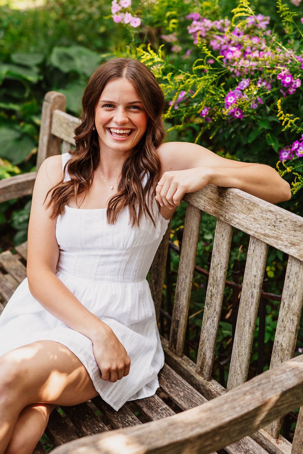 White summer dress shown against rustic wooden garden bench surrounded by colorful flowers.