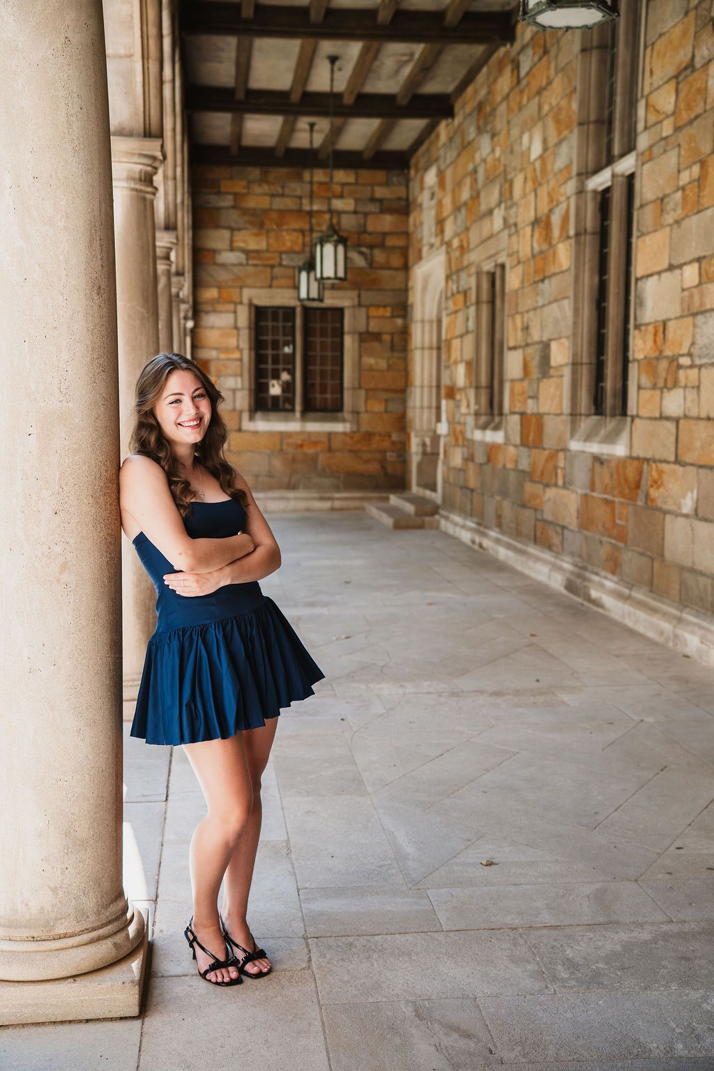 Multiple poses captured under a covered stone walkway featuring a navy blue summer dress and casual footwear.