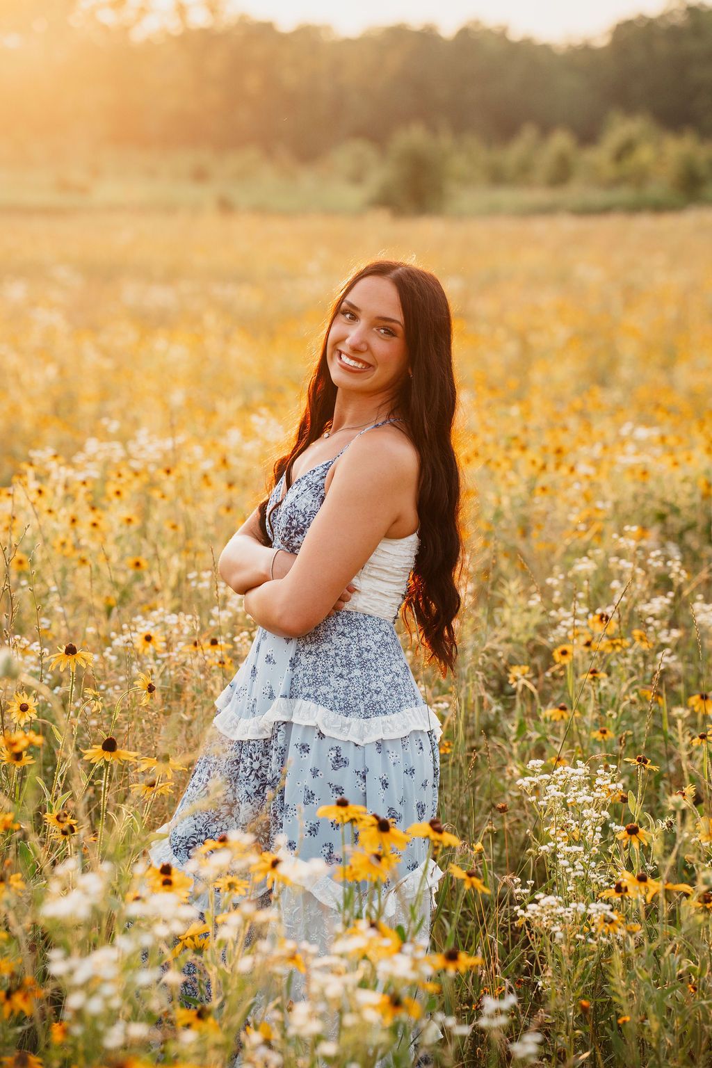Person in a patterned dress standing in a field of yellow and white wildflowers at dusk.