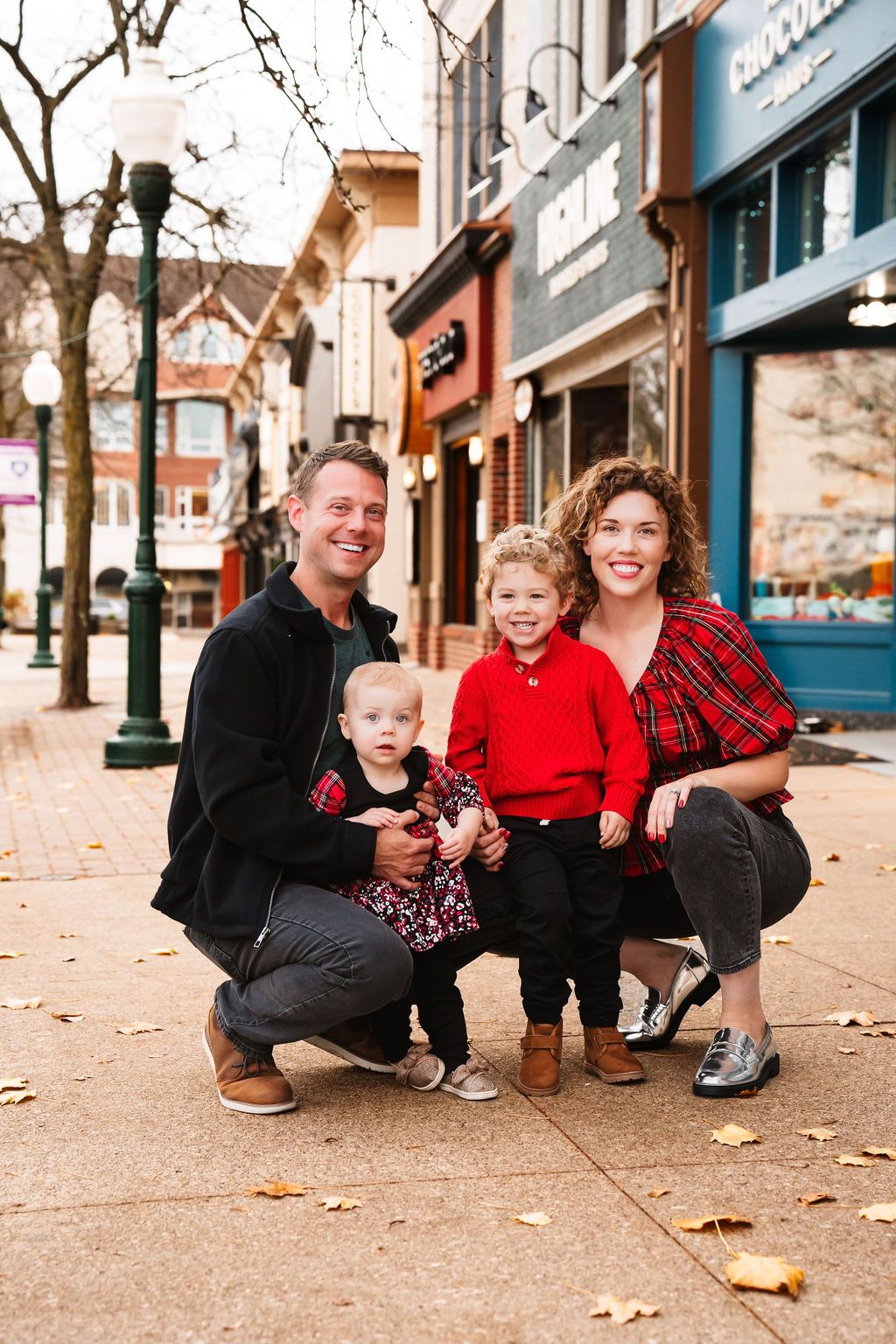 Holiday themed family portraits on city sidewalk with festive red and black outfits.