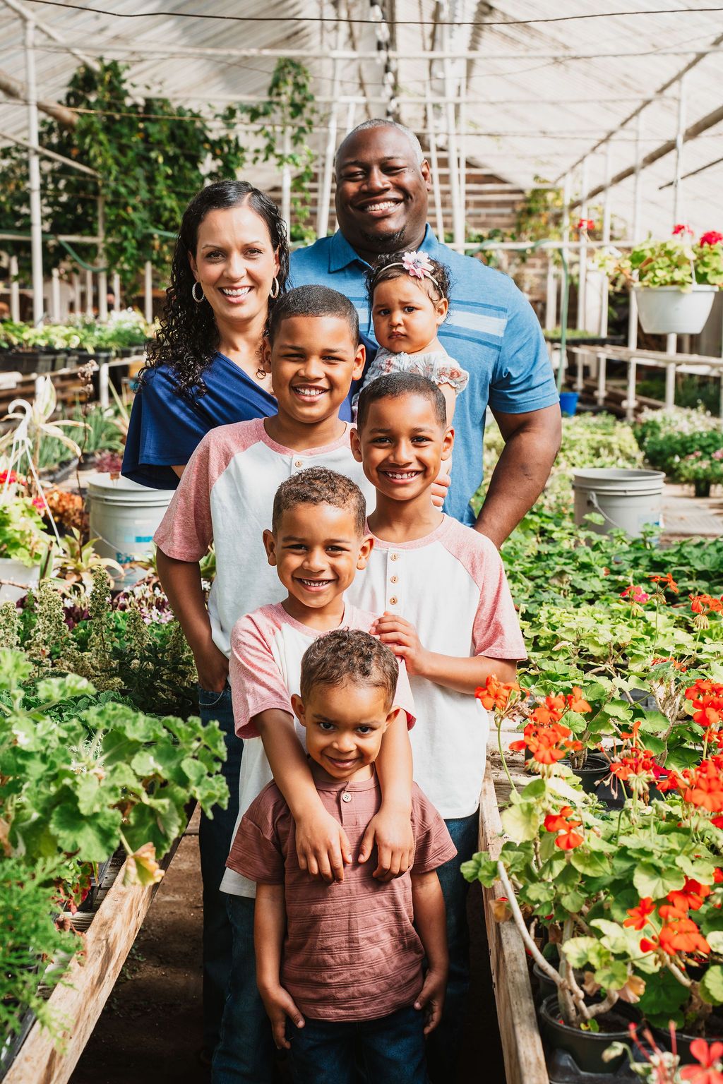 Happy family of six posing among colorful plants and flowers inside a garden greenhouse nursery.