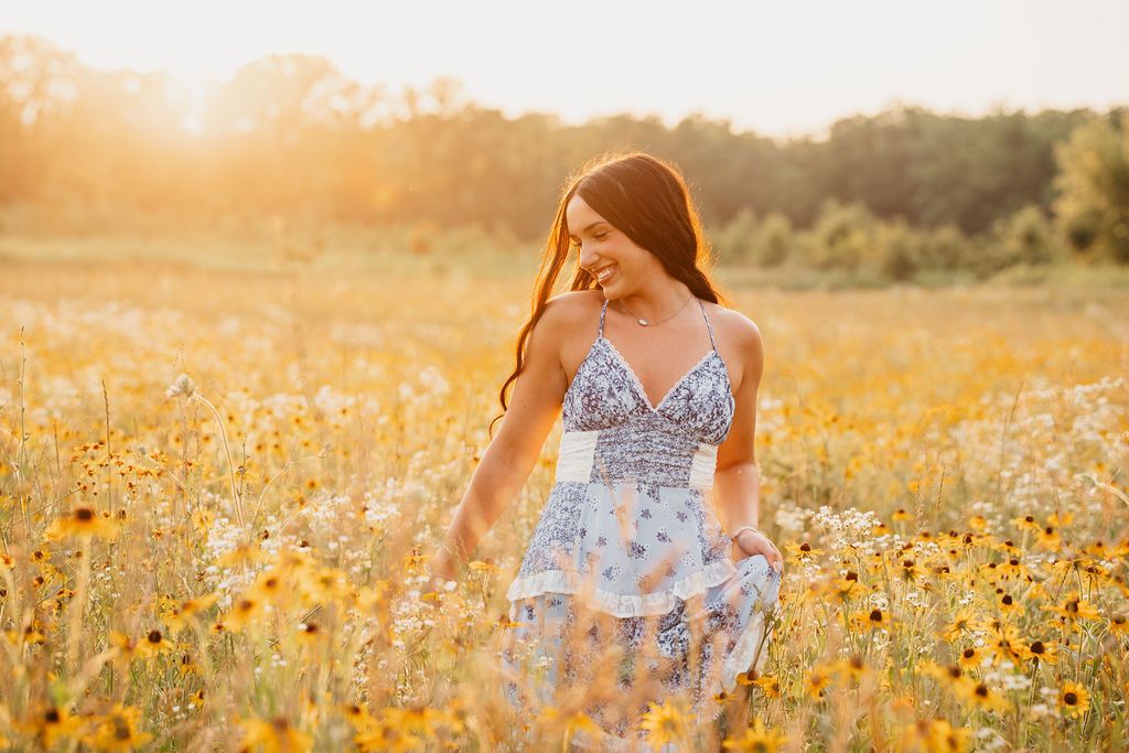 Woman in blue dress walking through golden wildflower field at sunset. canton wildflower field Michigan senior photos golden hour, Franklin