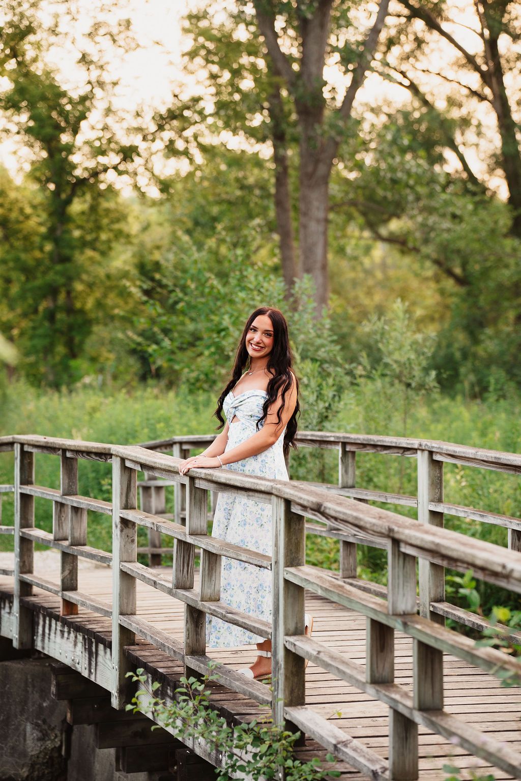 A summer portrait session on a rustic wooden bridge surrounded by trees and natural lighting.