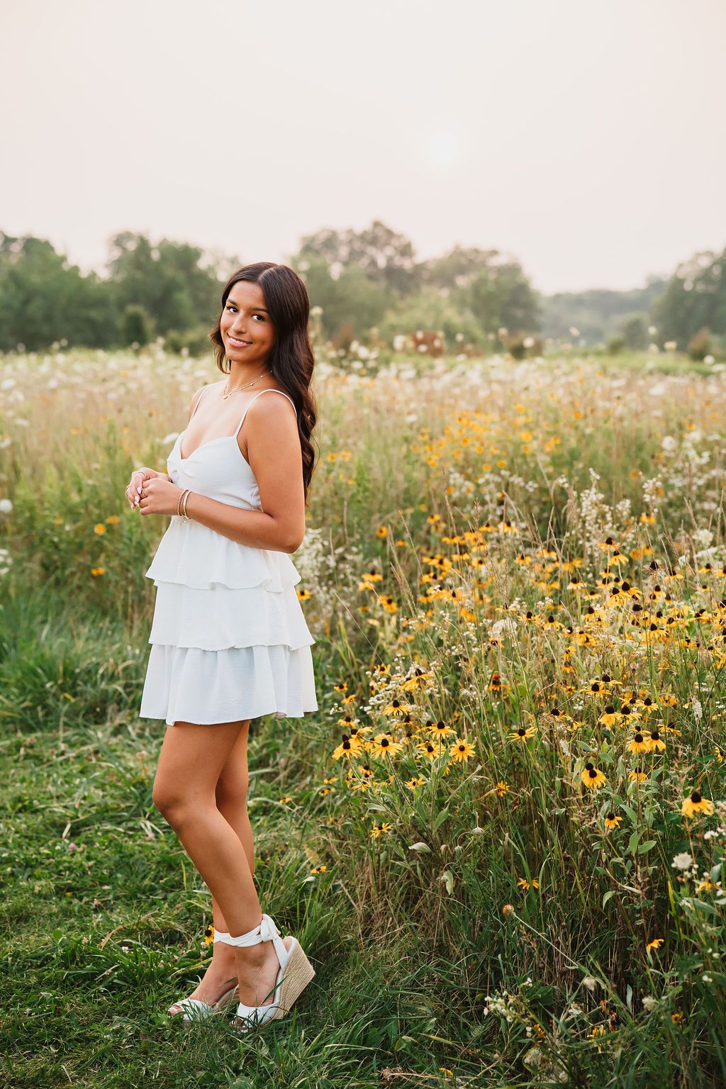 A white summer dress stands out against a golden meadow of wildflowers during a warm evening photoshoot.