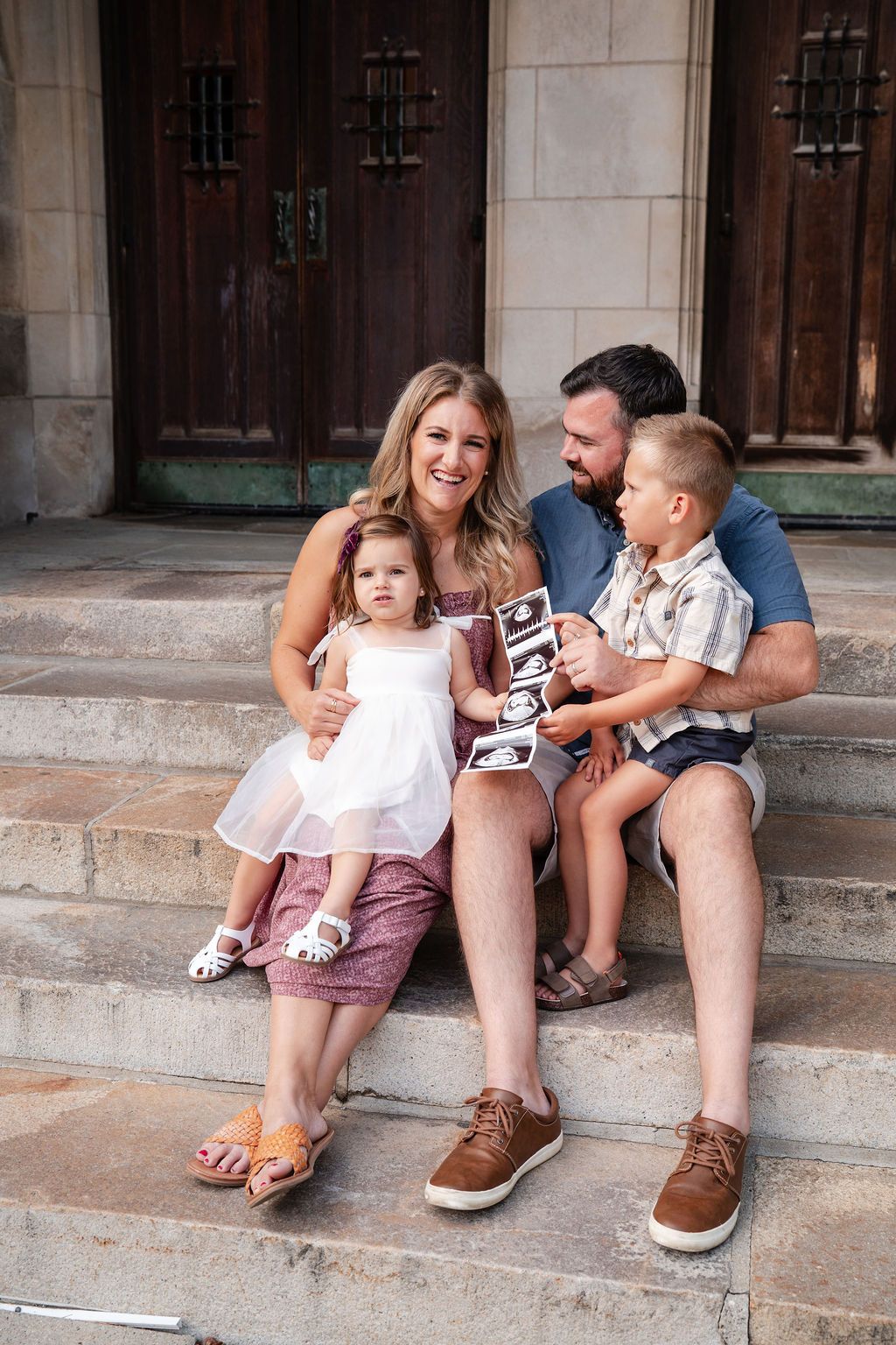 A family sits together on stone steps sharing ultrasound photos and tender moments.
