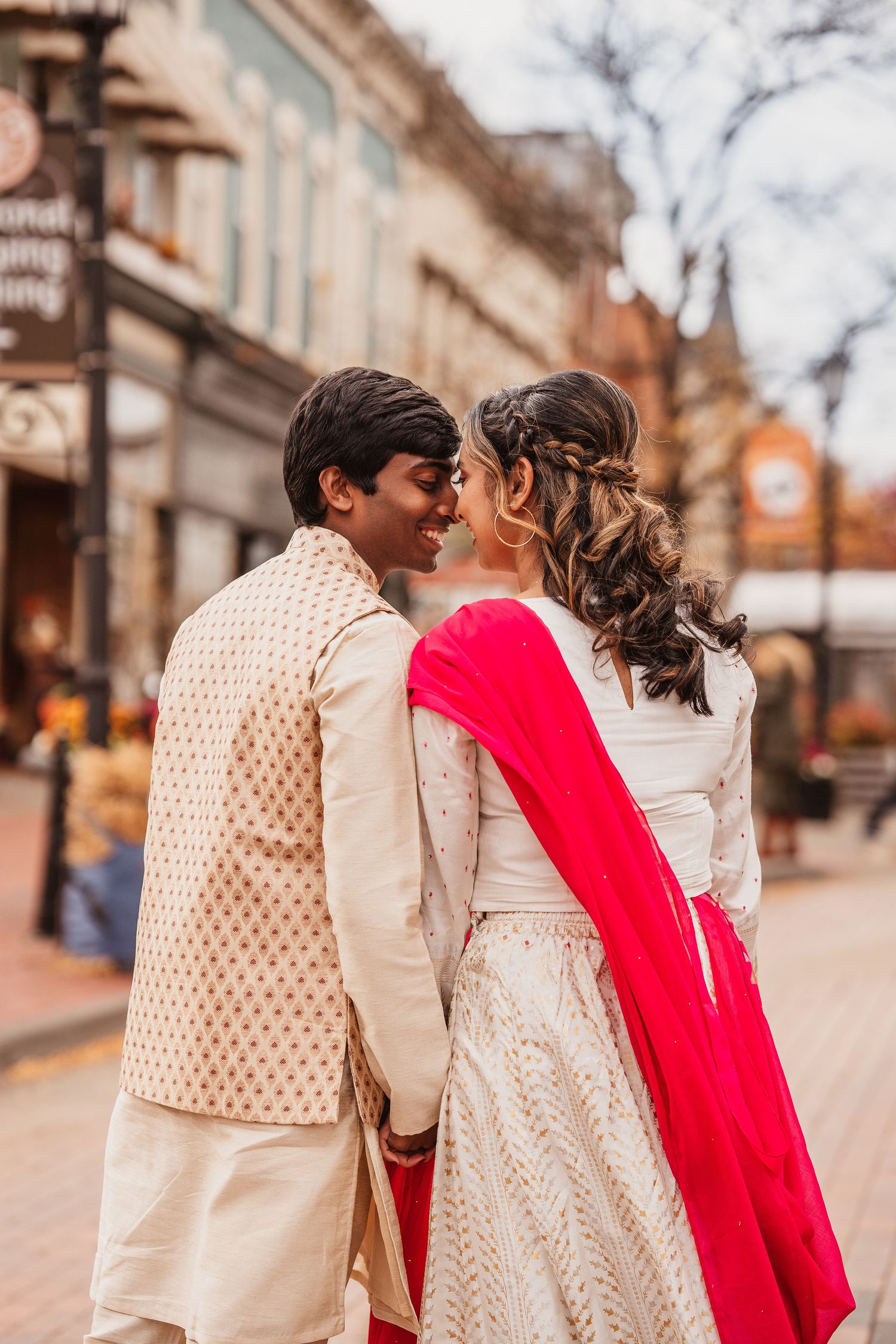 Couple in traditional Indian wedding attire sharing an intimate moment on a city street. engagement photos Northville Michigan