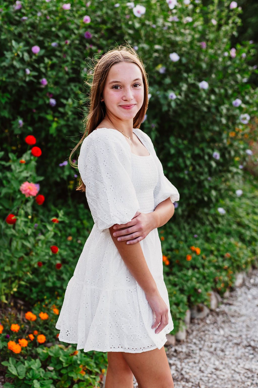 White eyelet dress photographed in a garden with blooming flowers and greenery.