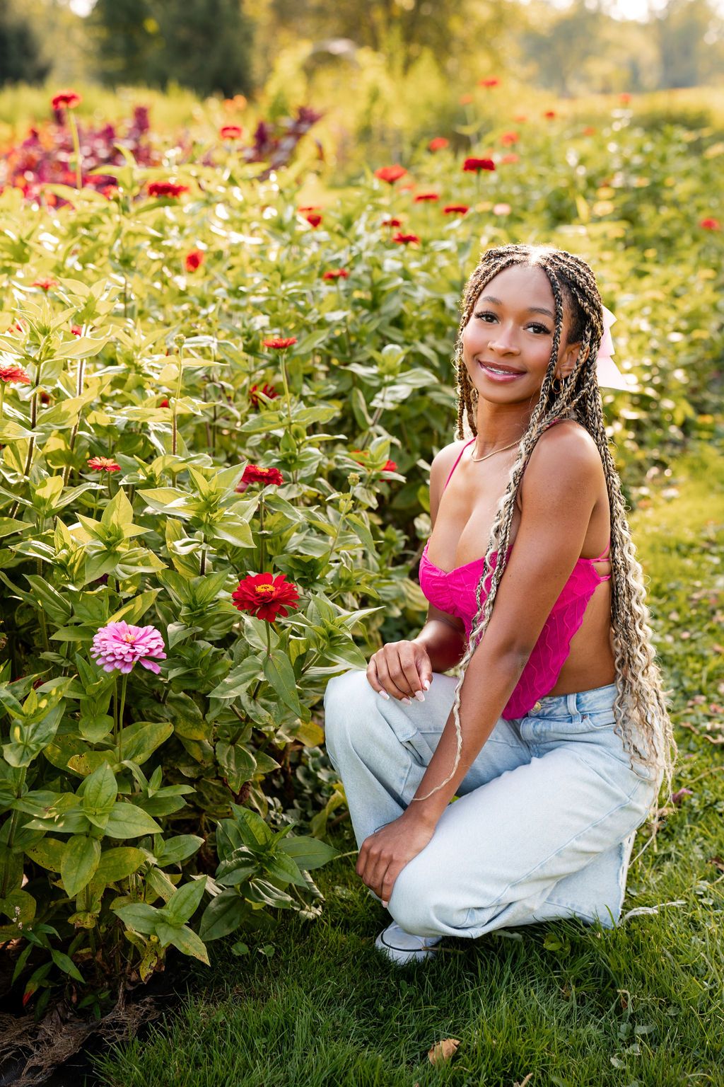 Person in pink top posing by blooming red zinnias in garden during golden hour. Fowl creek farms senior photos Michigan